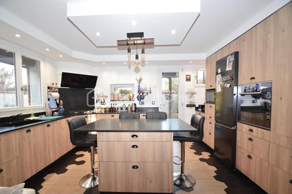 À Saint-Laurent-de-la-Salanque, laissez-vous séduire par cette superbe villa traditionnelle 3 faces de 180 m² habitables, nichée dans un quartier résidentiel calme, à proximité immédiate des commodités et à quelques minutes seulement des plages du Barcarès. Édifiée sur une parcelle de 465 m², elle offre un cadre de vie à la fois paisible et fonctionnel. Dès l'entrée, une allée paysagée mène à un porche fermé ouvrant sur un vaste hall. Le séjour lumineux, agrémenté d'une cheminée à foyer fermé, crée une atmosphère chaleureuse. La cuisine ouverte, de fabrication artisanale, séduit par son îlot central et ses finitions haut de gamme en granit noir, avec un accès direct à une terrasse semi-couverte idéale pour recevoir. Les extérieurs invitent à la détente avec piscine chauffée au sel exposée plein sud, espace barbecue et emplacement prévu pour un jacuzzi. Le rez-de-chaussée comprend également une chambre, une salle d'eau avec WC, un cellier et un garage. À l'étage, quatre grandes chambres avec rangements, dont une suite parentale, ainsi qu'une élégante salle de bain. Le dernier niveau offre une chambre supplémentaire et un bureau, parfaits pour le télétravail. Prestations complètes et confort moderne font de cette villa un bien rare, idéal pour une grande famille.