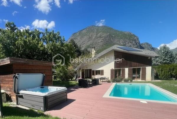 Amoureux des lieux atypiques, cette maison est faite pour vous.
Découvrez cette maison d’architecte de 191 m² habitables, offrant 7 pièces aux volumes généreux et aux espaces de vie chaleureux et lumineux, 
le tout implanté sur un terrain de 1 523 m². 
Elle se situe dans un secteur recherché, à proximité des commerces et des stations de ski de la Maurienne.
Exposée plein sud, cette propriété rénovée en 2020 bénéficie d’une belle luminosité naturelle et d’une architecture intérieure originale, 
idéale pour les amateurs de biens authentiques et de caractère.
Édifiée sur deux niveaux, elle séduit dès l’entrée par son vaste hall baigné de lumière, grâce à ses grandes baies vitrées.

Au rez-de-chaussée, vous découvrirez une cuisine entièrement équipée ouverte sur le séjour, avec accès direct à la terrasse extérieure. 
Une magnifique cheminée traversante double foyer vient harmonieusement séparer le séjour du salon, apportant charme et convivialité à l’ensemble.
Le séjour, sublimé par un parquet en bois massif, renforce le caractère chaleureux et raffiné de la maison.
Ce niveau comprend également deux chambres, dont une suite parentale avec salle d’eau privative et accès à une véranda équipée d’une cuisine, 
permettant si besoin de créer un espace indépendant.
Un coin buanderie ainsi qu’un WC séparé viennent compléter ce niveau.
Les belles hauteurs sous plafond et les nombreuses ouvertures accentuent la sensation d’espace et l’atmosphère conviviale de cette propriété unique.

Un élégant escalier mène à l’étage, où vous découvrirez trois chambres confortables, de 13 à 25 m², chacune sublimée par de magnifiques poutres apparentes, 
apportant charme et authenticité.
Vous y trouverez également une salle de bains familiale avec toilettes, ainsi qu’une superbe mezzanine de 25 m², 
habillée d’un parquet massif et aménagée en second salon, surplombant la pièce de vie du rez-de-chaussée et offrant une remarquable sensation d’espace et de volume.

Les extérieurs, soigneusement aménagés, offrent un véritable espace de détente et de convivialité. 
Vous profiterez d’une grande terrasse, d’une piscine au sel chauffée par pompe à chaleur, parfaitement intégrée avec sa terrasse en composite, 
d’un jacuzzi, ainsi que d’un chalet de jardin. 
Le terrain, entièrement clos et paysager, apporte calme et intimité à l’ensemble de la propriété.

Côté dépendances, ce bien dispose également d’un double garage, de deux caves ainsi que d’un carport pouvant accueillir jusqu’à trois véhicules.
Enfin, la maison est équipée de panneaux photovoltaïques, permettant de couvrir une grande partie de la consommation électrique du logement.