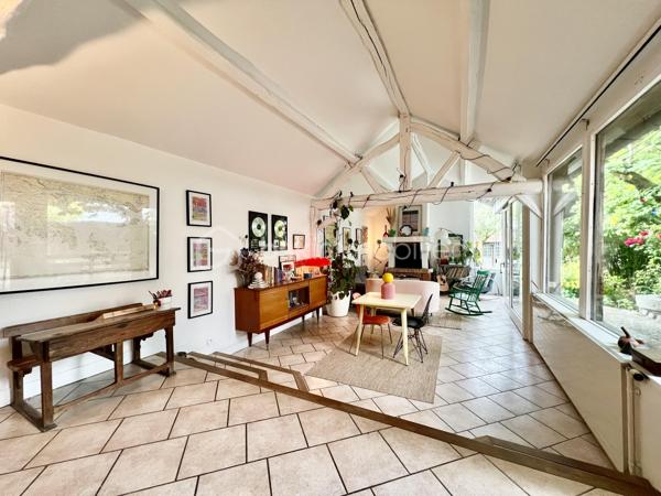 À proximité immédiate du centre-ville, des gares, des axes autoroutiers et de la tangentielle, cette authentique maison des années 1930 séduira les amoureux de cachet, d’espaces chaleureux et de projets de vie polyvalents.

Dès l’entrée, un couloir distribue : • une première chambre, • un toilette indépendant avec lave-mains, • une seconde chambre.
La visite se poursuit vers une cuisine récente, aménagée et équipée, ouverte sur une superbe extension baignée de lumière. Cette pièce de vie au charme incomparable offre une cheminée, une belle hauteur sous plafond et de magnifiques poutres apparentes. Grâce à ses larges ouvertures sur le jardin, l’intérieur et l’extérieur se répondent harmonieusement tout au long de l’année.

À l’étage, un palier aménagé en coin bibliothèque dessert : • une chambre, • une salle d’eau avec toilette, lavabo et bidet.
La maison bénéficie également d’un sous-sol complet comprenant plusieurs caves, une chaufferie ainsi qu’une pièce de 25 m² pouvant être aménagée en espace habitable, bureau indépendant, salle de loisirs ou studio selon vos besoins.

À l’extérieur, le jardin intimiste et arboré accueille : • un atelier indépendant d’environ 40 m², • deux garages de plus de 16 m² chacun, situés au fond du terrain, • une agréable terrasse ombragée par un magnifique tilleul.
Ces dépendances offrent un véritable potentiel pour une activité professionnelle ou un investissement locatif : atelier d’artiste, cabinet de profession libérale, espace de coworking, activité artisanale, stockage, studio indépendant ou bureaux.
Cette propriété conviendra parfaitement : • à un artisan souhaitant disposer d’un atelier à domicile, • à un artiste ou créatif recherchant un espace de travail indépendant, • à un professionnel libéral (architecte, thérapeute, coach, consultant, profession paramédicale…), • ou encore à un investisseur désirant exploiter les dépendances pour du locatif ou une activité complémentaire.

Une maison pleine d’âme et de possibilités, idéale pour conjuguer vie personnelle, activité professionnelle et projet patrimonial.

Taxe foncière: 2268€
Energie: 238€/mois