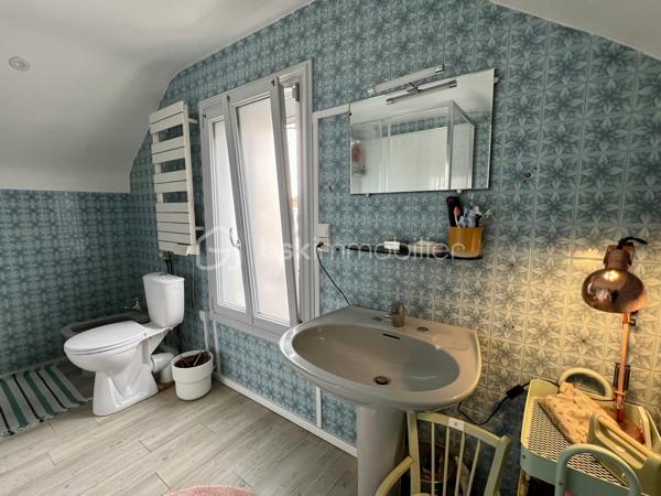 À proximité immédiate du centre-ville, des gares, des axes autoroutiers et de la tangentielle, cette authentique maison des années 1930 séduira les amoureux de cachet, d’espaces chaleureux et de projets de vie polyvalents.

Dès l’entrée, un couloir distribue : • une première chambre, • un toilette indépendant avec lave-mains, • une seconde chambre.
La visite se poursuit vers une cuisine récente, aménagée et équipée, ouverte sur une superbe extension baignée de lumière. Cette pièce de vie au charme incomparable offre une cheminée, une belle hauteur sous plafond et de magnifiques poutres apparentes. Grâce à ses larges ouvertures sur le jardin, l’intérieur et l’extérieur se répondent harmonieusement tout au long de l’année.

À l’étage, un palier aménagé en coin bibliothèque dessert : • une chambre, • une salle d’eau avec toilette, lavabo et bidet.
La maison bénéficie également d’un sous-sol complet comprenant plusieurs caves, une chaufferie ainsi qu’une pièce de 25 m² pouvant être aménagée en espace habitable, bureau indépendant, salle de loisirs ou studio selon vos besoins.

À l’extérieur, le jardin intimiste et arboré accueille : • un atelier indépendant d’environ 40 m², • deux garages de plus de 16 m² chacun, situés au fond du terrain, • une agréable terrasse ombragée par un magnifique tilleul.
Ces dépendances offrent un véritable potentiel pour une activité professionnelle ou un investissement locatif : atelier d’artiste, cabinet de profession libérale, espace de coworking, activité artisanale, stockage, studio indépendant ou bureaux.
Cette propriété conviendra parfaitement : • à un artisan souhaitant disposer d’un atelier à domicile, • à un artiste ou créatif recherchant un espace de travail indépendant, • à un professionnel libéral (architecte, thérapeute, coach, consultant, profession paramédicale…), • ou encore à un investisseur désirant exploiter les dépendances pour du locatif ou une activité complémentaire.

Une maison pleine d’âme et de possibilités, idéale pour conjuguer vie personnelle, activité professionnelle et projet patrimonial.

Taxe foncière: 2268€
Energie: 238€/mois