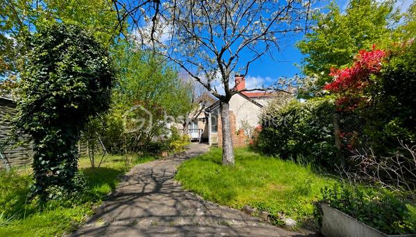 À proximité immédiate du centre-ville, des gares, des axes autoroutiers et de la tangentielle, cette authentique maison des années 1930 séduira les amoureux de cachet, d’espaces chaleureux et de projets de vie polyvalents.

Dès l’entrée, un couloir distribue : • une première chambre, • un toilette indépendant avec lave-mains, • une seconde chambre.
La visite se poursuit vers une cuisine récente, aménagée et équipée, ouverte sur une superbe extension baignée de lumière. Cette pièce de vie au charme incomparable offre une cheminée, une belle hauteur sous plafond et de magnifiques poutres apparentes. Grâce à ses larges ouvertures sur le jardin, l’intérieur et l’extérieur se répondent harmonieusement tout au long de l’année.

À l’étage, un palier aménagé en coin bibliothèque dessert : • une chambre, • une salle d’eau avec toilette, lavabo et bidet.
La maison bénéficie également d’un sous-sol complet comprenant plusieurs caves, une chaufferie ainsi qu’une pièce de 25 m² pouvant être aménagée en espace habitable, bureau indépendant, salle de loisirs ou studio selon vos besoins.

À l’extérieur, le jardin intimiste et arboré accueille : • un atelier indépendant d’environ 40 m², • deux garages de plus de 16 m² chacun, situés au fond du terrain, • une agréable terrasse ombragée par un magnifique tilleul.
Ces dépendances offrent un véritable potentiel pour une activité professionnelle ou un investissement locatif : atelier d’artiste, cabinet de profession libérale, espace de coworking, activité artisanale, stockage, studio indépendant ou bureaux.
Cette propriété conviendra parfaitement : • à un artisan souhaitant disposer d’un atelier à domicile, • à un artiste ou créatif recherchant un espace de travail indépendant, • à un professionnel libéral (architecte, thérapeute, coach, consultant, profession paramédicale…), • ou encore à un investisseur désirant exploiter les dépendances pour du locatif ou une activité complémentaire.

Une maison pleine d’âme et de possibilités, idéale pour conjuguer vie personnelle, activité professionnelle et projet patrimonial.

Taxe foncière: 2268€
Energie: 238€/mois