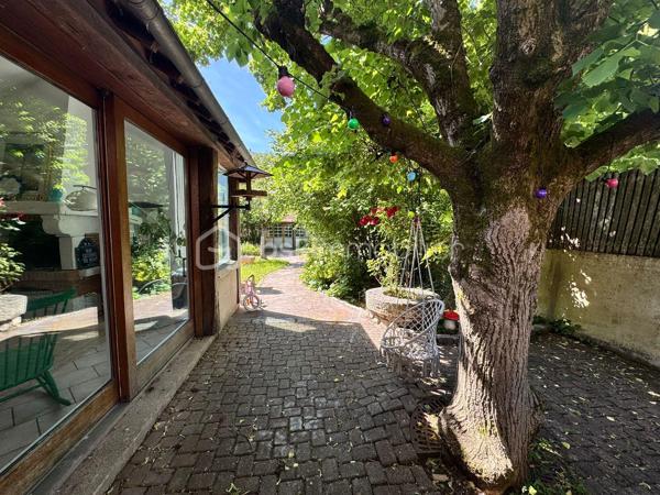 À proximité immédiate du centre-ville, des gares, des axes autoroutiers et de la tangentielle, cette authentique maison des années 1930 séduira les amoureux de cachet, d’espaces chaleureux et de projets de vie polyvalents.

Dès l’entrée, un couloir distribue : • une première chambre, • un toilette indépendant avec lave-mains, • une seconde chambre.
La visite se poursuit vers une cuisine récente, aménagée et équipée, ouverte sur une superbe extension baignée de lumière. Cette pièce de vie au charme incomparable offre une cheminée, une belle hauteur sous plafond et de magnifiques poutres apparentes. Grâce à ses larges ouvertures sur le jardin, l’intérieur et l’extérieur se répondent harmonieusement tout au long de l’année.

À l’étage, un palier aménagé en coin bibliothèque dessert : • une chambre, • une salle d’eau avec toilette, lavabo et bidet.
La maison bénéficie également d’un sous-sol complet comprenant plusieurs caves, une chaufferie ainsi qu’une pièce de 25 m² pouvant être aménagée en espace habitable, bureau indépendant, salle de loisirs ou studio selon vos besoins.

À l’extérieur, le jardin intimiste et arboré accueille : • un atelier indépendant d’environ 40 m², • deux garages de plus de 16 m² chacun, situés au fond du terrain, • une agréable terrasse ombragée par un magnifique tilleul.
Ces dépendances offrent un véritable potentiel pour une activité professionnelle ou un investissement locatif : atelier d’artiste, cabinet de profession libérale, espace de coworking, activité artisanale, stockage, studio indépendant ou bureaux.
Cette propriété conviendra parfaitement : • à un artisan souhaitant disposer d’un atelier à domicile, • à un artiste ou créatif recherchant un espace de travail indépendant, • à un professionnel libéral (architecte, thérapeute, coach, consultant, profession paramédicale…), • ou encore à un investisseur désirant exploiter les dépendances pour du locatif ou une activité complémentaire.

Une maison pleine d’âme et de possibilités, idéale pour conjuguer vie personnelle, activité professionnelle et projet patrimonial.

Taxe foncière: 2268€
Energie: 238€/mois