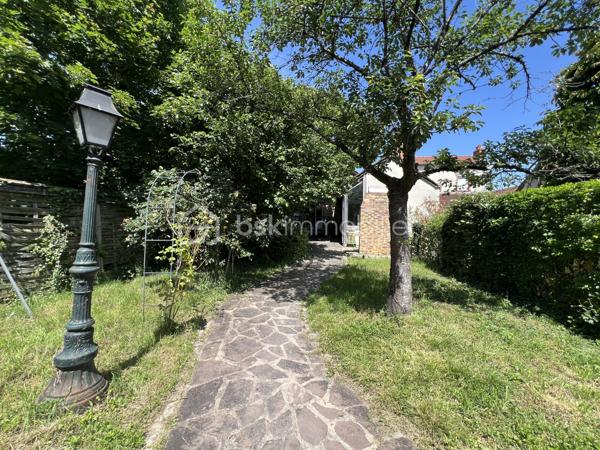 À proximité immédiate du centre-ville, des gares, des axes autoroutiers et de la tangentielle, cette authentique maison des années 1930 séduira les amoureux de cachet, d’espaces chaleureux et de projets de vie polyvalents.

Dès l’entrée, un couloir distribue : • une première chambre, • un toilette indépendant avec lave-mains, • une seconde chambre.
La visite se poursuit vers une cuisine récente, aménagée et équipée, ouverte sur une superbe extension baignée de lumière. Cette pièce de vie au charme incomparable offre une cheminée, une belle hauteur sous plafond et de magnifiques poutres apparentes. Grâce à ses larges ouvertures sur le jardin, l’intérieur et l’extérieur se répondent harmonieusement tout au long de l’année.

À l’étage, un palier aménagé en coin bibliothèque dessert : • une chambre, • une salle d’eau avec toilette, lavabo et bidet.
La maison bénéficie également d’un sous-sol complet comprenant plusieurs caves, une chaufferie ainsi qu’une pièce de 25 m² pouvant être aménagée en espace habitable, bureau indépendant, salle de loisirs ou studio selon vos besoins.

À l’extérieur, le jardin intimiste et arboré accueille : • un atelier indépendant d’environ 40 m², • deux garages de plus de 16 m² chacun, situés au fond du terrain, • une agréable terrasse ombragée par un magnifique tilleul.
Ces dépendances offrent un véritable potentiel pour une activité professionnelle ou un investissement locatif : atelier d’artiste, cabinet de profession libérale, espace de coworking, activité artisanale, stockage, studio indépendant ou bureaux.
Cette propriété conviendra parfaitement : • à un artisan souhaitant disposer d’un atelier à domicile, • à un artiste ou créatif recherchant un espace de travail indépendant, • à un professionnel libéral (architecte, thérapeute, coach, consultant, profession paramédicale…), • ou encore à un investisseur désirant exploiter les dépendances pour du locatif ou une activité complémentaire.

Une maison pleine d’âme et de possibilités, idéale pour conjuguer vie personnelle, activité professionnelle et projet patrimonial.

Taxe foncière: 2268€
Energie: 238€/mois