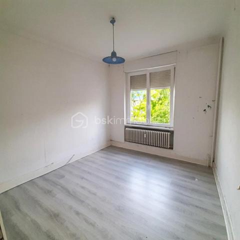 Situé au 3ᵉ étage du bâtiment annulaire, rue Auguste-Wicky à Mulhouse, cet appartement de 92 m² bénéficie d'un emplacement privilégié, à proximité immédiate de la gare et à deux pas du centre historique. Ses beaux volumes et sa configuration offrent de nombreuses possibilités d'aménagement.

Une adresse emblématique de Mulhouse
Construit dans les années 1950 par l'architecte Pierre-Jean Guth, le bâtiment annulaire est un édifice singulier de l'architecture mulhousienne d'après-guerre. Sa forme circulaire remarquable et son histoire lui ont valu une inscription au titre des monuments historiques en 2006. Une adresse de caractère, au cœur d'un ensemble architectural qui fait partie du patrimoine de la ville.

Un appartement à aménager selon votre projet
L'appartement se compose d'une large entrée, de quatre belles pièces de 11, 12, 16 et 17 m², offrant différentes possibilités d'aménagement selon les besoins de chacun. Une cuisine indépendante, une salle de bains, un WC séparé et un petit balcon complètent le bien.
Des travaux de rénovation sont à prévoir, laissant la possibilité de repenser les espaces et les prestations selon vos envies. Un devis a déjà été réalisé afin de permettre aux acquéreurs d'anticiper le budget nécessaire à leur projet.
À l'arrière de l'immeuble, la cour intérieure verdoyante entretenue par la Ville de Mulhouse apportent une touche de nature en milieu urbain. Le bien dispose également d'une cave. Des possibilités de stationnement existent à l'arrière de l'immeuble, sous réserve de disponibilité.

Que ce soit pour créer un lieu de vie personnalisé ou pour réaliser un investissement locatif, cet appartement présente un potentiel intéressant. Le règlement de copropriété autorise la location de courte durée, un atout supplémentaire pour les acquéreurs souhaitant étudier cette possibilité, sous réserve du respect de la réglementation applicable.

Informations complémentaires
- Surface : 92 m²
- Étage : 3ᵉ
- Chauffage collectif au gaz
- DPE : D — GES : D
- Taxe foncière : 1 200 € par an
- Charges annuelles comprennant charges générales de l'immeuble, eau chaude, eau froide et chauffage (5830€ de charges locatives sur 6283€ en 2025)
