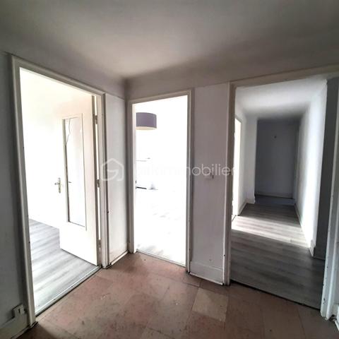 Situé au 3ᵉ étage du bâtiment annulaire, rue Auguste-Wicky à Mulhouse, cet appartement de 92 m² bénéficie d'un emplacement privilégié, à proximité immédiate de la gare et à deux pas du centre historique. Ses beaux volumes et sa configuration offrent de nombreuses possibilités d'aménagement.

Une adresse emblématique de Mulhouse
Construit dans les années 1950 par l'architecte Pierre-Jean Guth, le bâtiment annulaire est un édifice singulier de l'architecture mulhousienne d'après-guerre. Sa forme circulaire remarquable et son histoire lui ont valu une inscription au titre des monuments historiques en 2006. Une adresse de caractère, au cœur d'un ensemble architectural qui fait partie du patrimoine de la ville.

Un appartement à aménager selon votre projet
L'appartement se compose d'une large entrée, de quatre belles pièces de 11, 12, 16 et 17 m², offrant différentes possibilités d'aménagement selon les besoins de chacun. Une cuisine indépendante, une salle de bains, un WC séparé et un petit balcon complètent le bien.
Des travaux de rénovation sont à prévoir, laissant la possibilité de repenser les espaces et les prestations selon vos envies. Un devis a déjà été réalisé afin de permettre aux acquéreurs d'anticiper le budget nécessaire à leur projet.
À l'arrière de l'immeuble, la cour intérieure verdoyante entretenue par la Ville de Mulhouse apportent une touche de nature en milieu urbain. Le bien dispose également d'une cave. Des possibilités de stationnement existent à l'arrière de l'immeuble, sous réserve de disponibilité.

Que ce soit pour créer un lieu de vie personnalisé ou pour réaliser un investissement locatif, cet appartement présente un potentiel intéressant. Le règlement de copropriété autorise la location de courte durée, un atout supplémentaire pour les acquéreurs souhaitant étudier cette possibilité, sous réserve du respect de la réglementation applicable.

Informations complémentaires
- Surface : 92 m²
- Étage : 3ᵉ
- Chauffage collectif au gaz
- DPE : D — GES : D
- Taxe foncière : 1 200 € par an
- Charges annuelles comprennant charges générales de l'immeuble, eau chaude, eau froide et chauffage (5830€ de charges locatives sur 6283€ en 2025)