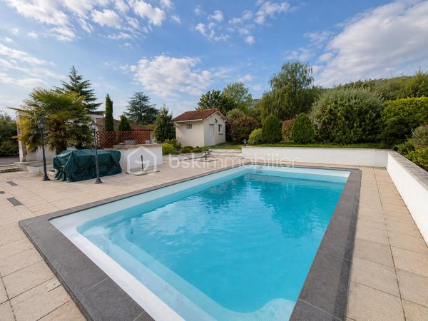 Construite en 1966 sur une belle parcelle close et arborée de 1 935 m², cette maison traditionnelle aux beaux volumes saura séduire les familles en quête d’espace, de confort et de tranquillité.

Dès l’arrivée, vous découvrirez un environnement agréable et verdoyant, sublimé par des extérieurs soigneusement aménagés avec piscine (8X4), pool house et vaste terrasse propice aux moments de convivialité.

Le rez-de-chaussée accueille un grand espace de réception avec coin bar et espace détente équipé d’un point d’eau, idéal pour recevoir famille et amis dans une ambiance conviviale. Cet espace donne directement accès à la terrasse et aux extérieurs. En demi-niveau et demi sous-sol, la maison dispose également d’une chambre avec salle d’eau, d’un WC séparé, d’une buanderie ainsi que de plusieurs espaces de rangement.

À l’étage, un couloir dessert une cuisine indépendante aménagée et équipée, un séjour lumineux, trois chambres, une salle de bain, un WC séparé ainsi que de nombreux placards et penderies.

Le chauffage est assuré par des radiateurs électriques complétés par le poêle à granulés installé dans l’espace de vie du rez-de-chaussée.

Côté annexes, le bien bénéficie d’un double garage avec cave à l’arrière, d’un atelier attenant à la maison et de combles perdus au-dessus.

Cette propriété offre un fort potentiel pour accueillir une grande famille, recevoir des proches ou simplement profiter d’un cadre de vie privilégié avec de beaux espaces intérieurs et extérieurs.

Un bien rare sur le secteur, alliant charme, fonctionnalité et qualité de vie.