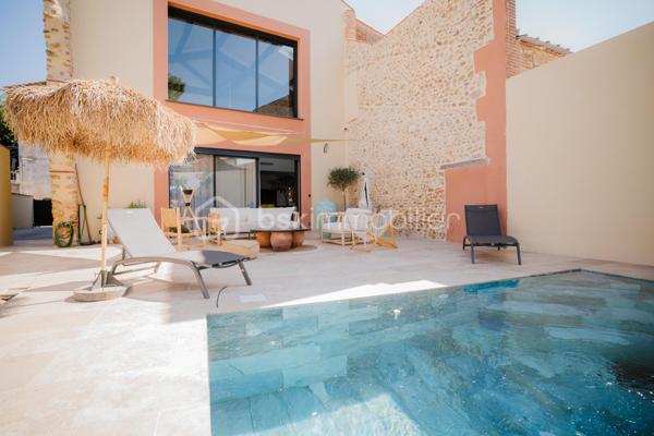 Bages (66) – Ancienne grange réinventée, volumes d’exception, piscine balinaise et grand garage

Au cœur de Bages, cette ancienne grange en pierre a fait l’objet d’une rénovation complète pour devenir une maison de caractère d’environ 250 m². Pierre apparente, briques et charpente en bois dialoguent avec des aménagements contemporains et des matériaux soigneusement choisis.

La pièce de vie constitue le cœur de la maison : 96 m² ouverts sur une hauteur sous plafond culminant à 8,50 mètres. Les grandes ouvertures et l’exposition Ouest donnent toute leur dimension à ces volumes remarquables. Salon, salle à manger et cuisine s’y organisent naturellement, offrant autant d’espace pour recevoir que pour partager le quotidien.

La cuisine, avec son îlot central, associe les tons chaleureux du bois à une crédence d’un vert profond. L’escalier et la mezzanine dessinent les perspectives de cet intérieur singulier, où le charme de l’ancien accompagne une rénovation résolument actuelle.

Côté nuit, la maison accueille cinq chambres, dont une suite parentale de 32m2 avec dressing et salle d’eau privative. Une grande salle de bains, un bureau et la mezzanine complètent l’ensemble, pour répondre aux besoins d’une famille comme au plaisir de recevoir.

À l’extérieur, la terrasse prolonge les espaces de vie dans une ambiance intime, sans vis-à-vis. Piscine balinaise, cuisine d’été et salon à l’ombre des voiles composent un cadre propice aux repas partagés et aux moments de détente. La propriété s’étend sur une parcelle de 594 m²

La climatisation gainable assure le chauffage et le rafraîchissement de l’habitation. Autre atout particulièrement appréciable : un garage d’environ 90 m², doté d’une belle hauteur sous plafond, d’une douche et d’un WC, offrant de nombreuses possibilités de stationnement et de rangement.

À proximité des commerces, des écoles et des services du village, cette maison conjugue une adresse pratique à Bages et un lieu de vie à forte personnalité, à quelques kilomètres de Perpignan.

En complément, possibilité d’acquérir un bâtiment de stockage composé de box, proposé séparément, pour un projet locatif ou des besoins d’espace supplémentaires. Renseignements sur demande.

Pour découvrir cette maison et apprécier pleinement ses volumes, contactez Patrick Martens au 06 44 07 22 82 BSK Immobilier.