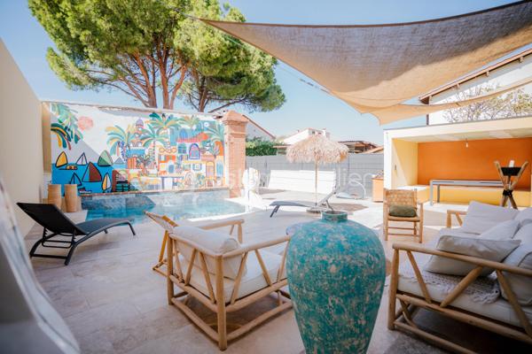 Bages (66) – Ancienne grange réinventée, volumes d’exception, piscine balinaise et grand garage

Au cœur de Bages, cette ancienne grange en pierre a fait l’objet d’une rénovation complète pour devenir une maison de caractère d’environ 250 m². Pierre apparente, briques et charpente en bois dialoguent avec des aménagements contemporains et des matériaux soigneusement choisis.

La pièce de vie constitue le cœur de la maison : 96 m² ouverts sur une hauteur sous plafond culminant à 8,50 mètres. Les grandes ouvertures et l’exposition Ouest donnent toute leur dimension à ces volumes remarquables. Salon, salle à manger et cuisine s’y organisent naturellement, offrant autant d’espace pour recevoir que pour partager le quotidien.

La cuisine, avec son îlot central, associe les tons chaleureux du bois à une crédence d’un vert profond. L’escalier et la mezzanine dessinent les perspectives de cet intérieur singulier, où le charme de l’ancien accompagne une rénovation résolument actuelle.

Côté nuit, la maison accueille cinq chambres, dont une suite parentale de 32m2 avec dressing et salle d’eau privative. Une grande salle de bains, un bureau et la mezzanine complètent l’ensemble, pour répondre aux besoins d’une famille comme au plaisir de recevoir.

À l’extérieur, la terrasse prolonge les espaces de vie dans une ambiance intime, sans vis-à-vis. Piscine balinaise, cuisine d’été et salon à l’ombre des voiles composent un cadre propice aux repas partagés et aux moments de détente. La propriété s’étend sur une parcelle de 594 m²

La climatisation gainable assure le chauffage et le rafraîchissement de l’habitation. Autre atout particulièrement appréciable : un garage d’environ 90 m², doté d’une belle hauteur sous plafond, d’une douche et d’un WC, offrant de nombreuses possibilités de stationnement et de rangement.

À proximité des commerces, des écoles et des services du village, cette maison conjugue une adresse pratique à Bages et un lieu de vie à forte personnalité, à quelques kilomètres de Perpignan.

En complément, possibilité d’acquérir un bâtiment de stockage composé de box, proposé séparément, pour un projet locatif ou des besoins d’espace supplémentaires. Renseignements sur demande.

Pour découvrir cette maison et apprécier pleinement ses volumes, contactez Patrick Martens au 06 44 07 22 82 BSK Immobilier.