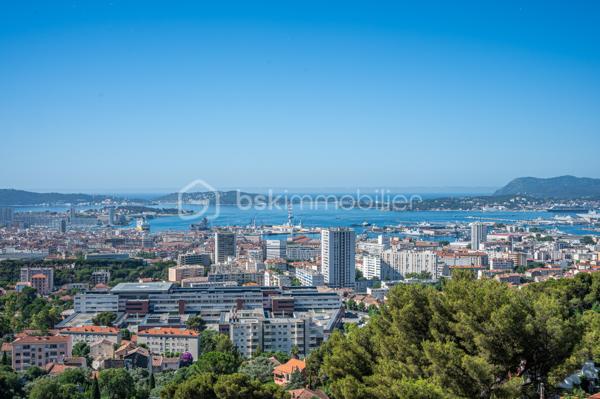 TOULON – FARON | Appartement-villa d’exception avec panorama sur la mer et la rade

Sur les hauteurs du Faron, au sein d’une copropriété de standing à l’architecture remarquable, ce bien rare occupe le dernier niveau et bénéficie d’un cadre de vie privilégié, entre mer, nature et élégance.

Véritable appartement-villa développé de plain-pied, il offre plus de 200 m² habitables sur un ensemble d’environ 1 000 m², en jouissance exclusive. Il conjugue le confort d’un appartement avec l’esprit d’une villa : volumes généreux, circulation fluide sur un seul niveau, accès privatif, extérieurs d’exception et piscine privative.

Dès l’entrée, le regard se laisse naturellement porter vers la Méditerranée. La mer, la rade de Toulon et les reliefs environnants dessinent un décor d’une rare intensité, visible depuis les espaces de réception comme depuis les extérieurs. Ici, le panorama ne se contemple pas seulement : il devient une composante essentielle de l’art de vivre offert par ce lieu unique.

Pensé autour d’un véritable art de vivre indoor-outdoor, ce bien offre une continuité rare entre intérieur et extérieur. Les espaces de réception se prolongent naturellement vers les terrasses, créant une atmosphère lumineuse, ouverte et entièrement tournée vers le panorama.

La pièce de vie, d’une superficie de plus de 75 m², constitue le cœur du bien. Ses belles proportions, sa cheminée et son ouverture direct à l’extérieur en font un espace à la fois élégant, chaleureux et convivial. La cuisine équipée s’inscrit dans le même esprit de confort et de raffinement.

L’espace nuit comprend trois chambres, dont une suite parentale avec salle de bains privative, ainsi qu’une seconde salle de bains et un bureau pouvant être aménagé en quatrième chambre. La distribution préserve l’intimité des espaces privés tout en conservant une circulation harmonieuse.

À l’extérieur, terrasses, jardin, piscine de 5 x 11 mètres, une cuisine d’été avec sanitaire, et une terrasse couverte. Ces espaces prolongent l’appartement comme une véritables pièces de vie à ciel ouvert, idéales pour recevoir, se détendre et de profiter pleinement du climat méditerranéen dans un cadre privilégié face à la mer et à l’une des plus belles rades du monde.

Un accès privatif, plusieurs emplacements de stationnement et deux caves complètent cet ensemble rare sur le marché toulonnais.

Ce bien réunit les atouts d’un appartement de standing — sécurité, dernier étage, vie de plain-pied — et le confort d’une villa, avec ses extérieurs généreux, sa piscine privative, son adresse confidentielle et l’absence de vis-à-vis.

Un bien unique sur le secteur du Faron, destiné à une clientèle recherchant un lieu de vie rare, élégant et résolument tourné vers l’art de vivre méditerranéen.

Des prestations soignées et haut de gamme complètent ce bien d’exception, avec chauffage individuel au gaz, climatisation réversible et système d’arrosage automatique, pour un confort optimal en toute saison.