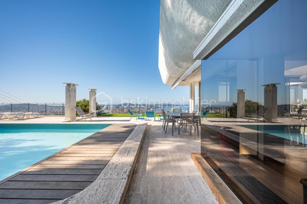TOULON – FARON | Appartement-villa d’exception avec panorama sur la mer et la rade

Sur les hauteurs du Faron, au sein d’une copropriété de standing à l’architecture remarquable, ce bien rare occupe le dernier niveau et bénéficie d’un cadre de vie privilégié, entre mer, nature et élégance.

Véritable appartement-villa développé de plain-pied, il offre plus de 200 m² habitables sur un ensemble d’environ 1 000 m², en jouissance exclusive. Il conjugue le confort d’un appartement avec l’esprit d’une villa : volumes généreux, circulation fluide sur un seul niveau, accès privatif, extérieurs d’exception et piscine privative.

Dès l’entrée, le regard se laisse naturellement porter vers la Méditerranée. La mer, la rade de Toulon et les reliefs environnants dessinent un décor d’une rare intensité, visible depuis les espaces de réception comme depuis les extérieurs. Ici, le panorama ne se contemple pas seulement : il devient une composante essentielle de l’art de vivre offert par ce lieu unique.

Pensé autour d’un véritable art de vivre indoor-outdoor, ce bien offre une continuité rare entre intérieur et extérieur. Les espaces de réception se prolongent naturellement vers les terrasses, créant une atmosphère lumineuse, ouverte et entièrement tournée vers le panorama.

La pièce de vie, d’une superficie de plus de 75 m², constitue le cœur du bien. Ses belles proportions, sa cheminée et son ouverture direct à l’extérieur en font un espace à la fois élégant, chaleureux et convivial. La cuisine équipée s’inscrit dans le même esprit de confort et de raffinement.

L’espace nuit comprend trois chambres, dont une suite parentale avec salle de bains privative, ainsi qu’une seconde salle de bains et un bureau pouvant être aménagé en quatrième chambre. La distribution préserve l’intimité des espaces privés tout en conservant une circulation harmonieuse.

À l’extérieur, terrasses, jardin, piscine de 5 x 11 mètres, une cuisine d’été avec sanitaire, et une terrasse couverte. Ces espaces prolongent l’appartement comme une véritables pièces de vie à ciel ouvert, idéales pour recevoir, se détendre et de profiter pleinement du climat méditerranéen dans un cadre privilégié face à la mer et à l’une des plus belles rades du monde.

Un accès privatif, plusieurs emplacements de stationnement et deux caves complètent cet ensemble rare sur le marché toulonnais.

Ce bien réunit les atouts d’un appartement de standing — sécurité, dernier étage, vie de plain-pied — et le confort d’une villa, avec ses extérieurs généreux, sa piscine privative, son adresse confidentielle et l’absence de vis-à-vis.

Un bien unique sur le secteur du Faron, destiné à une clientèle recherchant un lieu de vie rare, élégant et résolument tourné vers l’art de vivre méditerranéen.

Des prestations soignées et haut de gamme complètent ce bien d’exception, avec chauffage individuel au gaz, climatisation réversible et système d’arrosage automatique, pour un confort optimal en toute saison.