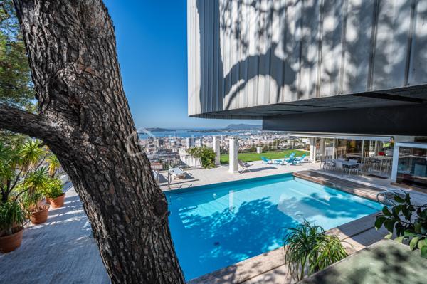 TOULON – FARON | Appartement-villa d’exception avec panorama sur la mer et la rade

Sur les hauteurs du Faron, au sein d’une copropriété de standing à l’architecture remarquable, ce bien rare occupe le dernier niveau et bénéficie d’un cadre de vie privilégié, entre mer, nature et élégance.

Véritable appartement-villa développé de plain-pied, il offre plus de 200 m² habitables sur un ensemble d’environ 1 000 m², en jouissance exclusive. Il conjugue le confort d’un appartement avec l’esprit d’une villa : volumes généreux, circulation fluide sur un seul niveau, accès privatif, extérieurs d’exception et piscine privative.

Dès l’entrée, le regard se laisse naturellement porter vers la Méditerranée. La mer, la rade de Toulon et les reliefs environnants dessinent un décor d’une rare intensité, visible depuis les espaces de réception comme depuis les extérieurs. Ici, le panorama ne se contemple pas seulement : il devient une composante essentielle de l’art de vivre offert par ce lieu unique.

Pensé autour d’un véritable art de vivre indoor-outdoor, ce bien offre une continuité rare entre intérieur et extérieur. Les espaces de réception se prolongent naturellement vers les terrasses, créant une atmosphère lumineuse, ouverte et entièrement tournée vers le panorama.

La pièce de vie, d’une superficie de plus de 75 m², constitue le cœur du bien. Ses belles proportions, sa cheminée et son ouverture direct à l’extérieur en font un espace à la fois élégant, chaleureux et convivial. La cuisine équipée s’inscrit dans le même esprit de confort et de raffinement.

L’espace nuit comprend trois chambres, dont une suite parentale avec salle de bains privative, ainsi qu’une seconde salle de bains et un bureau pouvant être aménagé en quatrième chambre. La distribution préserve l’intimité des espaces privés tout en conservant une circulation harmonieuse.

À l’extérieur, terrasses, jardin, piscine de 5 x 11 mètres, une cuisine d’été avec sanitaire, et une terrasse couverte. Ces espaces prolongent l’appartement comme une véritables pièces de vie à ciel ouvert, idéales pour recevoir, se détendre et de profiter pleinement du climat méditerranéen dans un cadre privilégié face à la mer et à l’une des plus belles rades du monde.

Un accès privatif, plusieurs emplacements de stationnement et deux caves complètent cet ensemble rare sur le marché toulonnais.

Ce bien réunit les atouts d’un appartement de standing — sécurité, dernier étage, vie de plain-pied — et le confort d’une villa, avec ses extérieurs généreux, sa piscine privative, son adresse confidentielle et l’absence de vis-à-vis.

Un bien unique sur le secteur du Faron, destiné à une clientèle recherchant un lieu de vie rare, élégant et résolument tourné vers l’art de vivre méditerranéen.

Des prestations soignées et haut de gamme complètent ce bien d’exception, avec chauffage individuel au gaz, climatisation réversible et système d’arrosage automatique, pour un confort optimal en toute saison.