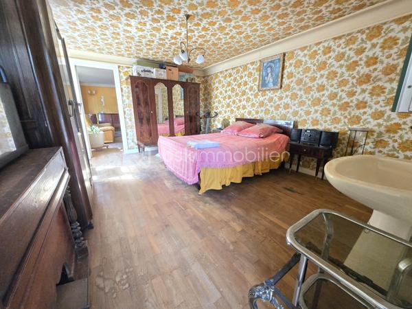 Au cœur du bourg, cette maison en pierre mitoyenne d’un côté offre une belle surface habitable, de nombreux espaces et un potentiel intéressant pour qui souhaite lui redonner une nouvelle vie.
Le rez-de-chaussée s’organise autour d’une entrée desservant une cuisine, une salle à manger, un salon, ainsi qu’une chambre avec point d’eau. Un dégagement mène également à un WC indépendant avec lavabo.
À l’étage, le palier dessert quatre chambres, une salle de bains, une salle d’eau et un second WC indépendant. Au-dessus, un grenier d’environ 35 m² vient compléter l’ensemble et offre une possibilité supplémentaire d’aménagement.
La maison a conservé son intérieur d’origine et nécessite aujourd’hui une rénovation et une remise au goût du jour, notamment pour la cuisine, les pièces d’eau, l’électricité et l’isolation. Le chauffage central au fioul est actuellement fonctionnel et l’installation dessert l’ensemble de la maison. 
À l’extérieur, les dépendances apportent un véritable atout avec une grange d’environ 65 m², une cave de 11,35 m², ainsi qu’un garage d’environ 30 m². Un cabanon, une terrasse et un jardin complètent la propriété, le tout sur un terrain d’environ 796 m².
Une maison qui offre avant tout une belle base et un véritable potentiel de transformation : les volumes sont là, les dépendances aussi, et les futurs propriétaires pourront progressivement la réinventer pour créer un intérieur à leur image.
Un bien à découvrir pour celles et ceux qui recherchent le charme de la pierre, de l’espace et un projet de rénovation à personnaliser.