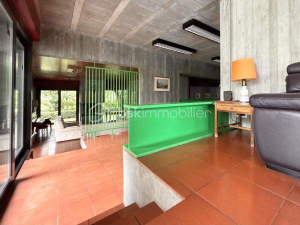bonjour. Voici l'essentiel : 
à Gières au fort du Mûrier, une villa-belvédère 
258 m2 habitables 
158 m2 locaux annexes
416 m2 surface utile
6 chambres
4 salles de bain
Piscine à débordement
Terrain arboré et clos : 6737 m2 (chemin de ronde partiellement)

Bienvenue à celles et ceux qui préfère emprunter le « chemin de ronde » architectural :
A l'aube des années 80, aucune entrave à l'audace de ces jeunes architectes et commanditaires qui saisissent cette exceptionnelle opportunité de construire cette villa-belvédère au flanc du Fort du Mûrier à Gières qui verrouille la vallée du Grésivaudan.
La villa lui emprunte sa matérialité, son ancrage et sa compacité qu'elle exprime par les outils architecturaux développés dans le sillage de Le Corbusier.
Là où le Fort retourne comme un gant l'alignement des façades de ses casemates en une rue utilitaire  encastrée, la villa, sous le ruban de la haute poutre-acrotère du toit-terrasse, déploie, par redents irréguliers, l'alternance de ses parois pleines et vitrées toute hauteur.
Elle exalte la minéralité de sa périphérie de terrasses gravillonnées, d'une brique nuancée appareillée horizontalement en pans ourlés et d'un béton aux épidermes multiples tantôt lisse, tantôt brut de décoffrage, parfois avec méplats mais toujours d'expression verticale et favorise sa vocation résidentielle par les nombreux et généreux pans vitrés de son rez-de-jardin de 222 m2 intégralement de plain-pied. 
A cette projection dans le paysage proche et lointain répond une fluidité intérieure autorisée par la prédilection des échappées visuelles obliques et un certain dépouillement général.
Au final,  sans en imposer mais avec fermeté, sans mimétisme au fort, par son inaltérable minimalisme, la villa-belvédère semble surgie hier autant que depuis des temps immémoriaux.

Une chambre d'écho aux bruissements des éléments, du végétal et de la montagne.
Comme le fort organise sa vie défensive en fonction de sa rue en boomerang, la villa répartit son organisation de part et d'autre d'une rue intérieure dotée de la même orientation nord-ouest/sud-est salutaire eu égard au réchauffement climatique. 
Au nord, l’espace nuit de hauteur conventionnelle comprend 4 chambres, 3 salles d’eau nimbées d'une subtile lumière zénithale et 2 wc. Toutes les chambres s'exonèrent d'une vue frontale sur le fort au profit d'orientations est et ouest plus agréables. La suite parentale outre le privilège de ses 27 m2 et sa baie cadrant les trois pics de Freydone, dispose d'un accès doublé par le salon surélevé. Arrêtons-nous sur cette pièce singulière qui jouit d'un rapport visuel immédiat avec le miroir d'eau sur lequel flotte la chaine de Belledonne...salon tour-à-tour empli de la rumeur ludique de la piscine et assurément contemplative la nuit ou aux aurores, sa triple ouverture et son surplomb du hall l'apparentent au campement à la « croisée des chemins »  ce dont atteste la ligne fuyant et sinueuse des ganivelles de châtaigner du chemin de ronde.

Au sud de la rue intérieure, avec laquelle ils partagent une hauteur sous plafond avoisinant les 3 mètres, se déploient les lieux de rassemblement ou de concentration que sont le séjour, la cuisine, la salle-à-manger et le bureau.
Le séjour en contrebas de la rue intérieure s'organise autour du bloc massif intégrant le foyer-insert et son alter-ego le barbecue de la terrasse couverte des repas de mi-saison et d'été. Son plafond de panneaux de chêne massif confère à la pièce une couleur acoustique propice aux confidences.
On peut qualifier la cuisine d'agora familiale tant son organisation centripète permet de s'y tenir bien au-delà de sa fonction première de préparation des repas. Sa table tout en transparence dissout la frontière entre cuisine et terrasse tandis que ses ouvertures cardinales en diagonale permettent un contrôle visuel de toute la propriété : l'arrivée des visiteurs, le chevreuil du chemin de ronde, le gazouillis des oiseaux proches. Et que dire de son mobilier minimaliste et inaltérable aux couleurs hédoniques qui répond à sa mission depuis un demi-siècle avec la même justesse ?
Le niveau bas -d'égale surface- est purement fonctionnel. Au nord-ouest et de plain-pied avec l'accès à la propriété, le vaste garage est accessible par 3 portes sectionnelles et donne accès à un studio. Du fait de l'encastrement dans la déclivité du terrain et donc totalement enterrés, vous trouvez les espaces techniques tels que -principalement- la filtration de la piscine à débordement, la chaufferie et sa chaudière Weishaupt, la conserverie-cave à vins, la buanderie, l'atelier. Les vides sanitaires hauteur d'homme et partiellement soustrait à la roche réservent des opportunités d'aménagement. 

La villa s'implante au sud de l'équerre formé par le chemin de ronde et en lisière du hameau -solitaire mais solidaire- dont elle se protège par un écran végétal et une certaine déclivité.
Prolongement naturel du demi-kilomètre que constitue le tour de la propriété, un escalier extérieur donne accès au toit-terrasse qui offre une vue panoramique à 360 degrés sur le Vercors, Grenoble, la dent de Crolles, le Grésivaudan, le Mont-blanc par beau temps et la chaine de Belledonne. 
La boucle du Fort du Mûrier passe au pied de la propriété et offre au cours de ses deux heures de marche une succession de panoramas, selon les randonneurs, « à coupe le souffle ».
Aux portes de Grenoble, Gières, bien desservie par la rocade nord-est et à la croisée de plusieurs domaines skiables rejoints en moins d'une demie-heure, elle est dotée de tous les commerces et services. Mais une telle adresse se mérite et il faut - depuis le bourg - gravir un dénivelé de plus de 200 mètres pour atteindre le Fort et la villa.

Alain CHIAUDANO & Régis HERBIN, l’héroïque binôme architectural 
Durant les deux années précédant la construction, les commanditaires ont affronté de nombreuses résistances à leur projet mais cela n'a entamé en rien ni leur envie de vivre en ce lieu solitaire et grandiose ni la conviction d'Alain Chiaudano d'un plateau de vie -« bunker » en lévitation- affranchi de toute enveloppe conventionnelle. Malheureusement, quelques mois avant l'ouverture du chantier, l'architecte est emporté par la maladie et c'est son ami et associé régis Herbin qui fera preuve d'abnégation et de respect mémoriel. Porté par l'encouragement sans faille des commanditaires, le jeune architecte livrera en 15 mois une œuvre unique où tout est calepiné, apparent, doté d'une science des rythmes, des épidermes et de l'espace qui n'est pas sans rappeler l'Atelier de Montrouge de la première heure ou le binôme Le Corbusier-Wogenscky. 
Les améliorations que les résidents lui ont prodigué au fil des ans, la belle patine des ouvrages et au final, l'absence de toute modification majeure témoignent de la pertinence des choix initiaux et attestent de son état impeccable.