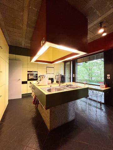 bonjour. Voici l'essentiel : 
à Gières au fort du Mûrier, une villa-belvédère 
258 m2 habitables 
158 m2 locaux annexes
416 m2 surface utile
6 chambres
4 salles de bain
Piscine à débordement
Terrain arboré et clos : 6737 m2 (chemin de ronde partiellement)

Bienvenue à celles et ceux qui préfère emprunter le « chemin de ronde » architectural :
A l'aube des années 80, aucune entrave à l'audace de ces jeunes architectes et commanditaires qui saisissent cette exceptionnelle opportunité de construire cette villa-belvédère au flanc du Fort du Mûrier à Gières qui verrouille la vallée du Grésivaudan.
La villa lui emprunte sa matérialité, son ancrage et sa compacité qu'elle exprime par les outils architecturaux développés dans le sillage de Le Corbusier.
Là où le Fort retourne comme un gant l'alignement des façades de ses casemates en une rue utilitaire  encastrée, la villa, sous le ruban de la haute poutre-acrotère du toit-terrasse, déploie, par redents irréguliers, l'alternance de ses parois pleines et vitrées toute hauteur.
Elle exalte la minéralité de sa périphérie de terrasses gravillonnées, d'une brique nuancée appareillée horizontalement en pans ourlés et d'un béton aux épidermes multiples tantôt lisse, tantôt brut de décoffrage, parfois avec méplats mais toujours d'expression verticale et favorise sa vocation résidentielle par les nombreux et généreux pans vitrés de son rez-de-jardin de 222 m2 intégralement de plain-pied. 
A cette projection dans le paysage proche et lointain répond une fluidité intérieure autorisée par la prédilection des échappées visuelles obliques et un certain dépouillement général.
Au final,  sans en imposer mais avec fermeté, sans mimétisme au fort, par son inaltérable minimalisme, la villa-belvédère semble surgie hier autant que depuis des temps immémoriaux.

Une chambre d'écho aux bruissements des éléments, du végétal et de la montagne.
Comme le fort organise sa vie défensive en fonction de sa rue en boomerang, la villa répartit son organisation de part et d'autre d'une rue intérieure dotée de la même orientation nord-ouest/sud-est salutaire eu égard au réchauffement climatique. 
Au nord, l’espace nuit de hauteur conventionnelle comprend 4 chambres, 3 salles d’eau nimbées d'une subtile lumière zénithale et 2 wc. Toutes les chambres s'exonèrent d'une vue frontale sur le fort au profit d'orientations est et ouest plus agréables. La suite parentale outre le privilège de ses 27 m2 et sa baie cadrant les trois pics de Freydone, dispose d'un accès doublé par le salon surélevé. Arrêtons-nous sur cette pièce singulière qui jouit d'un rapport visuel immédiat avec le miroir d'eau sur lequel flotte la chaine de Belledonne...salon tour-à-tour empli de la rumeur ludique de la piscine et assurément contemplative la nuit ou aux aurores, sa triple ouverture et son surplomb du hall l'apparentent au campement à la « croisée des chemins »  ce dont atteste la ligne fuyant et sinueuse des ganivelles de châtaigner du chemin de ronde.

Au sud de la rue intérieure, avec laquelle ils partagent une hauteur sous plafond avoisinant les 3 mètres, se déploient les lieux de rassemblement ou de concentration que sont le séjour, la cuisine, la salle-à-manger et le bureau.
Le séjour en contrebas de la rue intérieure s'organise autour du bloc massif intégrant le foyer-insert et son alter-ego le barbecue de la terrasse couverte des repas de mi-saison et d'été. Son plafond de panneaux de chêne massif confère à la pièce une couleur acoustique propice aux confidences.
On peut qualifier la cuisine d'agora familiale tant son organisation centripète permet de s'y tenir bien au-delà de sa fonction première de préparation des repas. Sa table tout en transparence dissout la frontière entre cuisine et terrasse tandis que ses ouvertures cardinales en diagonale permettent un contrôle visuel de toute la propriété : l'arrivée des visiteurs, le chevreuil du chemin de ronde, le gazouillis des oiseaux proches. Et que dire de son mobilier minimaliste et inaltérable aux couleurs hédoniques qui répond à sa mission depuis un demi-siècle avec la même justesse ?
Le niveau bas -d'égale surface- est purement fonctionnel. Au nord-ouest et de plain-pied avec l'accès à la propriété, le vaste garage est accessible par 3 portes sectionnelles et donne accès à un studio. Du fait de l'encastrement dans la déclivité du terrain et donc totalement enterrés, vous trouvez les espaces techniques tels que -principalement- la filtration de la piscine à débordement, la chaufferie et sa chaudière Weishaupt, la conserverie-cave à vins, la buanderie, l'atelier. Les vides sanitaires hauteur d'homme et partiellement soustrait à la roche réservent des opportunités d'aménagement. 

La villa s'implante au sud de l'équerre formé par le chemin de ronde et en lisière du hameau -solitaire mais solidaire- dont elle se protège par un écran végétal et une certaine déclivité.
Prolongement naturel du demi-kilomètre que constitue le tour de la propriété, un escalier extérieur donne accès au toit-terrasse qui offre une vue panoramique à 360 degrés sur le Vercors, Grenoble, la dent de Crolles, le Grésivaudan, le Mont-blanc par beau temps et la chaine de Belledonne. 
La boucle du Fort du Mûrier passe au pied de la propriété et offre au cours de ses deux heures de marche une succession de panoramas, selon les randonneurs, « à coupe le souffle ».
Aux portes de Grenoble, Gières, bien desservie par la rocade nord-est et à la croisée de plusieurs domaines skiables rejoints en moins d'une demie-heure, elle est dotée de tous les commerces et services. Mais une telle adresse se mérite et il faut - depuis le bourg - gravir un dénivelé de plus de 200 mètres pour atteindre le Fort et la villa.

Alain CHIAUDANO & Régis HERBIN, l’héroïque binôme architectural 
Durant les deux années précédant la construction, les commanditaires ont affronté de nombreuses résistances à leur projet mais cela n'a entamé en rien ni leur envie de vivre en ce lieu solitaire et grandiose ni la conviction d'Alain Chiaudano d'un plateau de vie -« bunker » en lévitation- affranchi de toute enveloppe conventionnelle. Malheureusement, quelques mois avant l'ouverture du chantier, l'architecte est emporté par la maladie et c'est son ami et associé régis Herbin qui fera preuve d'abnégation et de respect mémoriel. Porté par l'encouragement sans faille des commanditaires, le jeune architecte livrera en 15 mois une œuvre unique où tout est calepiné, apparent, doté d'une science des rythmes, des épidermes et de l'espace qui n'est pas sans rappeler l'Atelier de Montrouge de la première heure ou le binôme Le Corbusier-Wogenscky. 
Les améliorations que les résidents lui ont prodigué au fil des ans, la belle patine des ouvrages et au final, l'absence de toute modification majeure témoignent de la pertinence des choix initiaux et attestent de son état impeccable.