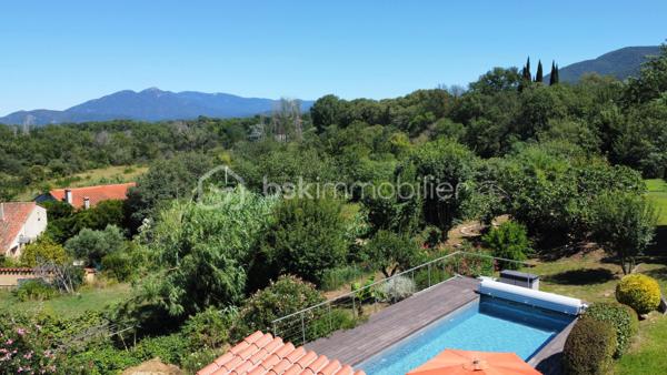 Dans un environnement verdoyant et avec des vues remarquables sur les Albères et le Pont du Diable, à 5 minutes du centre ville de Céret, cette villa vous offre un cadre de vie de nature tout en bénéficiant de la proximité de tous les services.
Édifiée sur un terrain de 2291 m2 auquel s’ajoutent 2 parcelles paysagères en espaliers de 1036 m2 et de 256 m2, la villa séduit par ses volumes généreux de 197,5 m2 habitables 
et 273 m2 utiles, ainsi que ses espaces espaces extérieurs sur plusieurs niveaux.
Au rez de chaussée, l’entrée s’ouvre sur l’espace de vie de 67 m2 incluant le séjour et sa cheminée exceptionnelle en pierre, le salon et la loggia aux vues splendides, ainsi qu’une grande cuisine déjeunatoire de 16 m2. 
L’espace nuit s’articule autour d’un couloir et ses rangements, avec 3 grandes chambres parquetées de 20, 13, 13 m2. 
Une salle d’eau/wc et des toilettes séparées complètent le rez de chaussée.
Au rez de jardin un studio indépendant de 29m2 avec coin cuisine, salle d’eau avec WC, et terrasse extérieure donnant sur la piscine. 
Idéal pour une grande famille ou l’opportunité de revenus locatifs.
Coté pratique, 3 espaces, cave, rangement, et cellier (54 m2 au total) et le garage de 21 m2 répondent à tous besoins de surface complémentaire.
À l’extérieur, une belle piscine de 9m x 3,5m, avec pompe à chaleur et volet électrique, d’un pool house couvert et d’une terrasse invitant à la convivialité dans une ambiance chaleureuse.
Offrant des vues dégagées sur le jardin et les Albères, un espace extérieur couvert de 44 m2 abrite un coin repas et un salon d’été parfaits pour partager des moments conviviaux.
La villa bénéficie de nombreux équipements rénovés :
Cuisine, salle d’eau et WC, piscine, toiture des 2 abris extérieurs, climatisation et pompes à chaleur, porte automatique de garage, motorisation des portails, volets roulants, alarme, loggia.
L’eau chaude est produite par des panneaux solaires.
La présence de 2 sources sur le terrain est un atout appréciable.
Stationnement pour plusieurs voitures.
Ce bien chaleureux et fonctionnel, bénéficiant de vues dégagées, est idéalement situé et agréable toute l’année