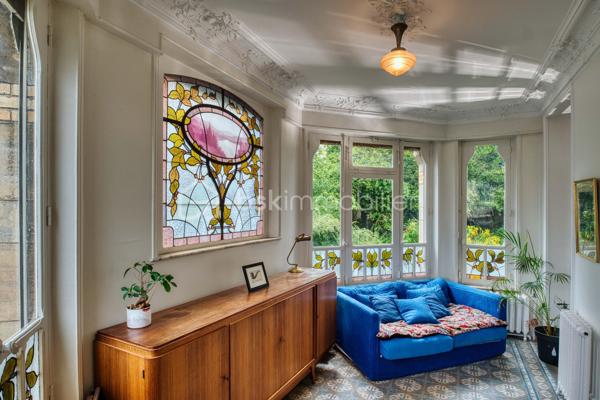 nouveau prix 775 000 euros FAI
Bienvenue dans cette villa, œuvre architecturale de Fernand César (1886-1969), associé et fils de l’architecte Félicien (1849-1930) livrée en 1912 à son commanditaire - l’industriel Adrien Humblot spécialiste de l’impression photographique - dans l’état que nous lui connaissons aujourd’hui. Elle sera habitée par François Streiff, doyen de la faculté de médecine et spécialiste de l’histoire artistique lorraine avant de l’être discrètement par les propriétaires actuels.

Toutes les façades -objet d’un soin architectural sans ostentation- s’articulent les unes aux autres avec bonheur par l’usage approprié du pan cassé. La façade sur rue sait exploiter le dénivelé sur rue et en profondeur grâce à l’horizontale du mur de clôture puis de soutènement en opus incertum de « mosaïque de roche ». Les éléments verticaux que sont la tour octogonale et la discrète entrée (que l’on dirait maçonnique) « écrivent » l’immeuble entre art nouveau et éclectisme.
1909, année de sa conception, correspond au chant du cygne du mouvement de l’École de Nancy. Les César sont reconnus pour une production architecturale polymorphe tant à Nancy, qu’à Vittel. Dès 1905 le fils seconde son père et s’en affranchit peu à peu mais continue de collaborer avec les artisans art nouveau de la seconde génération- ce qui ne manque pas de donner à cette villa toute sa singularité de dépouillement, de transition,  et de prélude à l’art déco dont nous fêtons le centenaire. 
Les interventions d’arts appliqués sont donc remarquablement mesurées : ferronneries, ébénisteries, céramiques, staff. Sauf celles de Jacques Gruber, qui foisonnent en un florilège de lumières, de compositions savantes au thème végétal et d’excellence des techniques mises en œuvre : grisailles, verres martelés, cabochons, gravures à l’acide…
Rappelons que le prolifique maître-verrier nancéien est l’auteur de vitraux pour la Chambre de Commerce et d’Industrie, la villa Majorelle et - avec les mêmes César - de l’immense verrière du siège nancéiens du Crédit Lyonnais.  

SUR UN PLAN PLUS TECHNIQUE…
Parlons chiffres d’abord : 
La surface utile totale est de 482 m2 décomposée ainsi :
Habitable : 315 m2
Annexes en sous-sol : 132 m2
Annexes aux étages et combles (compris surf. Planchers) : 35 m2
Non compris les surfaces de terrasses : 76 m2 (hors deck du jardin)
La contenance cadastrale est de 738 m2 développés en cœur d’ilot en jouxtant l’atelier sanctuarisé ayant vu la création du camouflage.
La consommation énergétique effectivement constatée sur base des factures est de 8000 à 8500 € l’an comprenant la production d’eau chaude sanitaire par cumulus électriques, le chauffage central produit par chaudière fuel et une consommation de bois d’environ 2 stères : bien loin des 20 000 € moyens issus du DPE. Malgré la médiocrité des performances théoriques, la maison s’avère confortable du fait de l’inertie de ses corps de chauffe surdimensionnés mais je ne peux cependant passer sous silence un comble démuni en période caniculaire mais qu’il serait aisé d’améliorer.
A la faveur de la récente rénovation, les réseaux électriques -intégralement encastrés- ont été renouvelés et complétés par un appareillage atemporel de boutons tournants.
La sécurité de la maison est assurée par détecteurs volumétriques et caméra pilotable.
Les revêtements de sol sont principalement de carreau en grès incrusté de Landrecies ou de parquet de chêne à pose en chevron. Les escaliers sont en comblanchien et doté de garde-corps en fer forgé. L’intervention contemporaine concerne le sol de béton peint des combles, le renforcement de toutes les canalisations et d’installations sanitaires supplémentaires.
La cuisine a fait l’objet d’un renouvellement récent par de nombreux agencements fonctionnels servis par de belles matières simples et nobles.
La maison dispose d’une telle quantité d’espaces servants en sous-sol et répartis aux étages que le mobilier peut être réduit à l’essentiel. 
Les dimensions généreuses du garage d’une hauteur supérieure à 270 cm lui permettent de stationner simultanément une berline voire un utilitaire et une moto. Le tout protégés par les vantaux d’origine coulissants, robustes et motorisés.

MAIS PLACE A LA VISITE !
Le rez-de-chaussée -réduit à sa fonction d’entrée- est mis en relation avec le bien-nommé « piano nobile » par un escalier vertigineusement théâtral qui nous amène directement au bureau.  Puis nous accédons à ce vaste hall central qui distribue les espaces de réception par un couple de portes à galandage vitrées qui favorisent ainsi avec la salle à-manger et le salon un espace de réception de quasiment 60 m2 voire de 75 m2 en ouvrant le jardin d’hiver. La partie fixe d’une salle-à-manger supposée d’Eugène Vallin côtoie une cheminée de gré émaillé de la maison Gentil-Bourdet et voit son radiateur équipé d’un chauffe-plat. Enfin, ce rez-de-jardin surélevé dispose de deux accès aux extérieurs, l’un par la cuisine et l’autre par le divin jardin d’hiver.
L’étage est doté d’une même hauteur sous plafond de 330 cm d’une même distribution centrée qui distribue 3 chambres, un immense dressing et la buanderie.
L’ascension se poursuit aux combles dotés de nombreuses surprises tel ce palier à l’énigmatique puits de lumière, cette chambre féeriquement monacale, une cabine de douche prodiguant musique chromothérapie et fonction de hammam et, encore plus inattendue, l’improbable roof-top de 50 m2 qui offre une vue panoramique sur la vieille ville et, par beau temps, jusqu’à la ligne bleue des Vosges.
Sur les deux niveaux nuit, la moitié des six chambres a une surface supérieure à 20 m2 et deux d’entre elles partagent une terrasse donnant sur le hêtre centenaire. La chambre parentale – 30 m2 compris sa salle d’eau privative- s’offre une triple orientation.
En résumé, avec une science consommée des harmonies, Fernand César offre une composition cruciforme de pièces toutes diversement personnalisées dans leurs proportions et qualifications (notamment par une dizaine de poêles et cheminées historiques) qui tire le meilleur parti de la course du soleil, du rapport équilibré au jardin arboré et des éléments qui y bruissent.
Parviendrons-nous - par nos mots et photographies- à restituer l’extrême pérennité des choix constructif de la villa, sa sobriété, gage d’une densité patrimoniale qui ne pèse jamais mais dont la consistance historique fait que chaque endroit du plus modeste au plus en vue témoigne avec simplicité de ce savoir-faire nancéien exceptionnel.

Hâte donc de vous y recevoir !

« Je voudrais de la lumière
Comme en Nouvelle Angleterre
Je veux changer d'atmosphère
Dans mon jardin d'hiver »