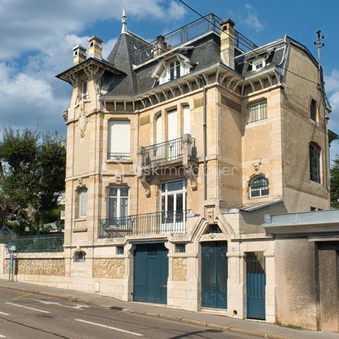 nouveau prix 775 000 euros FAI
Bienvenue dans cette villa, œuvre architecturale de Fernand César (1886-1969), associé et fils de l’architecte Félicien (1849-1930) livrée en 1912 à son commanditaire - l’industriel Adrien Humblot spécialiste de l’impression photographique - dans l’état que nous lui connaissons aujourd’hui. Elle sera habitée par François Streiff, doyen de la faculté de médecine et spécialiste de l’histoire artistique lorraine avant de l’être discrètement par les propriétaires actuels.

Toutes les façades -objet d’un soin architectural sans ostentation- s’articulent les unes aux autres avec bonheur par l’usage approprié du pan cassé. La façade sur rue sait exploiter le dénivelé sur rue et en profondeur grâce à l’horizontale du mur de clôture puis de soutènement en opus incertum de « mosaïque de roche ». Les éléments verticaux que sont la tour octogonale et la discrète entrée (que l’on dirait maçonnique) « écrivent » l’immeuble entre art nouveau et éclectisme.
1909, année de sa conception, correspond au chant du cygne du mouvement de l’École de Nancy. Les César sont reconnus pour une production architecturale polymorphe tant à Nancy, qu’à Vittel. Dès 1905 le fils seconde son père et s’en affranchit peu à peu mais continue de collaborer avec les artisans art nouveau de la seconde génération- ce qui ne manque pas de donner à cette villa toute sa singularité de dépouillement, de transition,  et de prélude à l’art déco dont nous fêtons le centenaire. 
Les interventions d’arts appliqués sont donc remarquablement mesurées : ferronneries, ébénisteries, céramiques, staff. Sauf celles de Jacques Gruber, qui foisonnent en un florilège de lumières, de compositions savantes au thème végétal et d’excellence des techniques mises en œuvre : grisailles, verres martelés, cabochons, gravures à l’acide…
Rappelons que le prolifique maître-verrier nancéien est l’auteur de vitraux pour la Chambre de Commerce et d’Industrie, la villa Majorelle et - avec les mêmes César - de l’immense verrière du siège nancéiens du Crédit Lyonnais.  

SUR UN PLAN PLUS TECHNIQUE…
Parlons chiffres d’abord : 
La surface utile totale est de 482 m2 décomposée ainsi :
Habitable : 315 m2
Annexes en sous-sol : 132 m2
Annexes aux étages et combles (compris surf. Planchers) : 35 m2
Non compris les surfaces de terrasses : 76 m2 (hors deck du jardin)
La contenance cadastrale est de 738 m2 développés en cœur d’ilot en jouxtant l’atelier sanctuarisé ayant vu la création du camouflage.
La consommation énergétique effectivement constatée sur base des factures est de 8000 à 8500 € l’an comprenant la production d’eau chaude sanitaire par cumulus électriques, le chauffage central produit par chaudière fuel et une consommation de bois d’environ 2 stères : bien loin des 20 000 € moyens issus du DPE. Malgré la médiocrité des performances théoriques, la maison s’avère confortable du fait de l’inertie de ses corps de chauffe surdimensionnés mais je ne peux cependant passer sous silence un comble démuni en période caniculaire mais qu’il serait aisé d’améliorer.
A la faveur de la récente rénovation, les réseaux électriques -intégralement encastrés- ont été renouvelés et complétés par un appareillage atemporel de boutons tournants.
La sécurité de la maison est assurée par détecteurs volumétriques et caméra pilotable.
Les revêtements de sol sont principalement de carreau en grès incrusté de Landrecies ou de parquet de chêne à pose en chevron. Les escaliers sont en comblanchien et doté de garde-corps en fer forgé. L’intervention contemporaine concerne le sol de béton peint des combles, le renforcement de toutes les canalisations et d’installations sanitaires supplémentaires.
La cuisine a fait l’objet d’un renouvellement récent par de nombreux agencements fonctionnels servis par de belles matières simples et nobles.
La maison dispose d’une telle quantité d’espaces servants en sous-sol et répartis aux étages que le mobilier peut être réduit à l’essentiel. 
Les dimensions généreuses du garage d’une hauteur supérieure à 270 cm lui permettent de stationner simultanément une berline voire un utilitaire et une moto. Le tout protégés par les vantaux d’origine coulissants, robustes et motorisés.

MAIS PLACE A LA VISITE !
Le rez-de-chaussée -réduit à sa fonction d’entrée- est mis en relation avec le bien-nommé « piano nobile » par un escalier vertigineusement théâtral qui nous amène directement au bureau.  Puis nous accédons à ce vaste hall central qui distribue les espaces de réception par un couple de portes à galandage vitrées qui favorisent ainsi avec la salle à-manger et le salon un espace de réception de quasiment 60 m2 voire de 75 m2 en ouvrant le jardin d’hiver. La partie fixe d’une salle-à-manger supposée d’Eugène Vallin côtoie une cheminée de gré émaillé de la maison Gentil-Bourdet et voit son radiateur équipé d’un chauffe-plat. Enfin, ce rez-de-jardin surélevé dispose de deux accès aux extérieurs, l’un par la cuisine et l’autre par le divin jardin d’hiver.
L’étage est doté d’une même hauteur sous plafond de 330 cm d’une même distribution centrée qui distribue 3 chambres, un immense dressing et la buanderie.
L’ascension se poursuit aux combles dotés de nombreuses surprises tel ce palier à l’énigmatique puits de lumière, cette chambre féeriquement monacale, une cabine de douche prodiguant musique chromothérapie et fonction de hammam et, encore plus inattendue, l’improbable roof-top de 50 m2 qui offre une vue panoramique sur la vieille ville et, par beau temps, jusqu’à la ligne bleue des Vosges.
Sur les deux niveaux nuit, la moitié des six chambres a une surface supérieure à 20 m2 et deux d’entre elles partagent une terrasse donnant sur le hêtre centenaire. La chambre parentale – 30 m2 compris sa salle d’eau privative- s’offre une triple orientation.
En résumé, avec une science consommée des harmonies, Fernand César offre une composition cruciforme de pièces toutes diversement personnalisées dans leurs proportions et qualifications (notamment par une dizaine de poêles et cheminées historiques) qui tire le meilleur parti de la course du soleil, du rapport équilibré au jardin arboré et des éléments qui y bruissent.
Parviendrons-nous - par nos mots et photographies- à restituer l’extrême pérennité des choix constructif de la villa, sa sobriété, gage d’une densité patrimoniale qui ne pèse jamais mais dont la consistance historique fait que chaque endroit du plus modeste au plus en vue témoigne avec simplicité de ce savoir-faire nancéien exceptionnel.

Hâte donc de vous y recevoir !

« Je voudrais de la lumière
Comme en Nouvelle Angleterre
Je veux changer d'atmosphère
Dans mon jardin d'hiver »