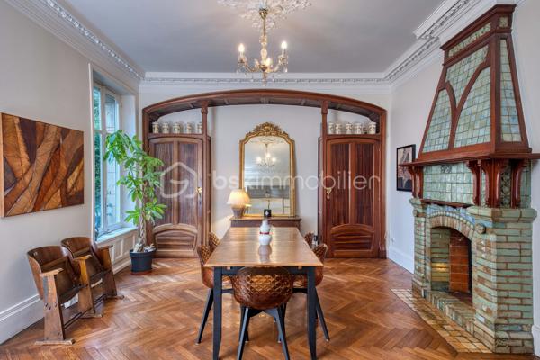 nouveau prix 775 000 euros FAI
Bienvenue dans cette villa, œuvre architecturale de Fernand César (1886-1969), associé et fils de l’architecte Félicien (1849-1930) livrée en 1912 à son commanditaire - l’industriel Adrien Humblot spécialiste de l’impression photographique - dans l’état que nous lui connaissons aujourd’hui. Elle sera habitée par François Streiff, doyen de la faculté de médecine et spécialiste de l’histoire artistique lorraine avant de l’être discrètement par les propriétaires actuels.

Toutes les façades -objet d’un soin architectural sans ostentation- s’articulent les unes aux autres avec bonheur par l’usage approprié du pan cassé. La façade sur rue sait exploiter le dénivelé sur rue et en profondeur grâce à l’horizontale du mur de clôture puis de soutènement en opus incertum de « mosaïque de roche ». Les éléments verticaux que sont la tour octogonale et la discrète entrée (que l’on dirait maçonnique) « écrivent » l’immeuble entre art nouveau et éclectisme.
1909, année de sa conception, correspond au chant du cygne du mouvement de l’École de Nancy. Les César sont reconnus pour une production architecturale polymorphe tant à Nancy, qu’à Vittel. Dès 1905 le fils seconde son père et s’en affranchit peu à peu mais continue de collaborer avec les artisans art nouveau de la seconde génération- ce qui ne manque pas de donner à cette villa toute sa singularité de dépouillement, de transition,  et de prélude à l’art déco dont nous fêtons le centenaire. 
Les interventions d’arts appliqués sont donc remarquablement mesurées : ferronneries, ébénisteries, céramiques, staff. Sauf celles de Jacques Gruber, qui foisonnent en un florilège de lumières, de compositions savantes au thème végétal et d’excellence des techniques mises en œuvre : grisailles, verres martelés, cabochons, gravures à l’acide…
Rappelons que le prolifique maître-verrier nancéien est l’auteur de vitraux pour la Chambre de Commerce et d’Industrie, la villa Majorelle et - avec les mêmes César - de l’immense verrière du siège nancéiens du Crédit Lyonnais.  

SUR UN PLAN PLUS TECHNIQUE…
Parlons chiffres d’abord : 
La surface utile totale est de 482 m2 décomposée ainsi :
Habitable : 315 m2
Annexes en sous-sol : 132 m2
Annexes aux étages et combles (compris surf. Planchers) : 35 m2
Non compris les surfaces de terrasses : 76 m2 (hors deck du jardin)
La contenance cadastrale est de 738 m2 développés en cœur d’ilot en jouxtant l’atelier sanctuarisé ayant vu la création du camouflage.
La consommation énergétique effectivement constatée sur base des factures est de 8000 à 8500 € l’an comprenant la production d’eau chaude sanitaire par cumulus électriques, le chauffage central produit par chaudière fuel et une consommation de bois d’environ 2 stères : bien loin des 20 000 € moyens issus du DPE. Malgré la médiocrité des performances théoriques, la maison s’avère confortable du fait de l’inertie de ses corps de chauffe surdimensionnés mais je ne peux cependant passer sous silence un comble démuni en période caniculaire mais qu’il serait aisé d’améliorer.
A la faveur de la récente rénovation, les réseaux électriques -intégralement encastrés- ont été renouvelés et complétés par un appareillage atemporel de boutons tournants.
La sécurité de la maison est assurée par détecteurs volumétriques et caméra pilotable.
Les revêtements de sol sont principalement de carreau en grès incrusté de Landrecies ou de parquet de chêne à pose en chevron. Les escaliers sont en comblanchien et doté de garde-corps en fer forgé. L’intervention contemporaine concerne le sol de béton peint des combles, le renforcement de toutes les canalisations et d’installations sanitaires supplémentaires.
La cuisine a fait l’objet d’un renouvellement récent par de nombreux agencements fonctionnels servis par de belles matières simples et nobles.
La maison dispose d’une telle quantité d’espaces servants en sous-sol et répartis aux étages que le mobilier peut être réduit à l’essentiel. 
Les dimensions généreuses du garage d’une hauteur supérieure à 270 cm lui permettent de stationner simultanément une berline voire un utilitaire et une moto. Le tout protégés par les vantaux d’origine coulissants, robustes et motorisés.

MAIS PLACE A LA VISITE !
Le rez-de-chaussée -réduit à sa fonction d’entrée- est mis en relation avec le bien-nommé « piano nobile » par un escalier vertigineusement théâtral qui nous amène directement au bureau.  Puis nous accédons à ce vaste hall central qui distribue les espaces de réception par un couple de portes à galandage vitrées qui favorisent ainsi avec la salle à-manger et le salon un espace de réception de quasiment 60 m2 voire de 75 m2 en ouvrant le jardin d’hiver. La partie fixe d’une salle-à-manger supposée d’Eugène Vallin côtoie une cheminée de gré émaillé de la maison Gentil-Bourdet et voit son radiateur équipé d’un chauffe-plat. Enfin, ce rez-de-jardin surélevé dispose de deux accès aux extérieurs, l’un par la cuisine et l’autre par le divin jardin d’hiver.
L’étage est doté d’une même hauteur sous plafond de 330 cm d’une même distribution centrée qui distribue 3 chambres, un immense dressing et la buanderie.
L’ascension se poursuit aux combles dotés de nombreuses surprises tel ce palier à l’énigmatique puits de lumière, cette chambre féeriquement monacale, une cabine de douche prodiguant musique chromothérapie et fonction de hammam et, encore plus inattendue, l’improbable roof-top de 50 m2 qui offre une vue panoramique sur la vieille ville et, par beau temps, jusqu’à la ligne bleue des Vosges.
Sur les deux niveaux nuit, la moitié des six chambres a une surface supérieure à 20 m2 et deux d’entre elles partagent une terrasse donnant sur le hêtre centenaire. La chambre parentale – 30 m2 compris sa salle d’eau privative- s’offre une triple orientation.
En résumé, avec une science consommée des harmonies, Fernand César offre une composition cruciforme de pièces toutes diversement personnalisées dans leurs proportions et qualifications (notamment par une dizaine de poêles et cheminées historiques) qui tire le meilleur parti de la course du soleil, du rapport équilibré au jardin arboré et des éléments qui y bruissent.
Parviendrons-nous - par nos mots et photographies- à restituer l’extrême pérennité des choix constructif de la villa, sa sobriété, gage d’une densité patrimoniale qui ne pèse jamais mais dont la consistance historique fait que chaque endroit du plus modeste au plus en vue témoigne avec simplicité de ce savoir-faire nancéien exceptionnel.

Hâte donc de vous y recevoir !

« Je voudrais de la lumière
Comme en Nouvelle Angleterre
Je veux changer d'atmosphère
Dans mon jardin d'hiver »