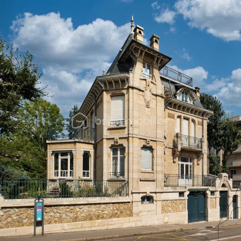 nouveau prix 775 000 euros FAI
Bienvenue dans cette villa, œuvre architecturale de Fernand César (1886-1969), associé et fils de l’architecte Félicien (1849-1930) livrée en 1912 à son commanditaire - l’industriel Adrien Humblot spécialiste de l’impression photographique - dans l’état que nous lui connaissons aujourd’hui. Elle sera habitée par François Streiff, doyen de la faculté de médecine et spécialiste de l’histoire artistique lorraine avant de l’être discrètement par les propriétaires actuels.

Toutes les façades -objet d’un soin architectural sans ostentation- s’articulent les unes aux autres avec bonheur par l’usage approprié du pan cassé. La façade sur rue sait exploiter le dénivelé sur rue et en profondeur grâce à l’horizontale du mur de clôture puis de soutènement en opus incertum de « mosaïque de roche ». Les éléments verticaux que sont la tour octogonale et la discrète entrée (que l’on dirait maçonnique) « écrivent » l’immeuble entre art nouveau et éclectisme.
1909, année de sa conception, correspond au chant du cygne du mouvement de l’École de Nancy. Les César sont reconnus pour une production architecturale polymorphe tant à Nancy, qu’à Vittel. Dès 1905 le fils seconde son père et s’en affranchit peu à peu mais continue de collaborer avec les artisans art nouveau de la seconde génération- ce qui ne manque pas de donner à cette villa toute sa singularité de dépouillement, de transition,  et de prélude à l’art déco dont nous fêtons le centenaire. 
Les interventions d’arts appliqués sont donc remarquablement mesurées : ferronneries, ébénisteries, céramiques, staff. Sauf celles de Jacques Gruber, qui foisonnent en un florilège de lumières, de compositions savantes au thème végétal et d’excellence des techniques mises en œuvre : grisailles, verres martelés, cabochons, gravures à l’acide…
Rappelons que le prolifique maître-verrier nancéien est l’auteur de vitraux pour la Chambre de Commerce et d’Industrie, la villa Majorelle et - avec les mêmes César - de l’immense verrière du siège nancéiens du Crédit Lyonnais.  

SUR UN PLAN PLUS TECHNIQUE…
Parlons chiffres d’abord : 
La surface utile totale est de 482 m2 décomposée ainsi :
Habitable : 315 m2
Annexes en sous-sol : 132 m2
Annexes aux étages et combles (compris surf. Planchers) : 35 m2
Non compris les surfaces de terrasses : 76 m2 (hors deck du jardin)
La contenance cadastrale est de 738 m2 développés en cœur d’ilot en jouxtant l’atelier sanctuarisé ayant vu la création du camouflage.
La consommation énergétique effectivement constatée sur base des factures est de 8000 à 8500 € l’an comprenant la production d’eau chaude sanitaire par cumulus électriques, le chauffage central produit par chaudière fuel et une consommation de bois d’environ 2 stères : bien loin des 20 000 € moyens issus du DPE. Malgré la médiocrité des performances théoriques, la maison s’avère confortable du fait de l’inertie de ses corps de chauffe surdimensionnés mais je ne peux cependant passer sous silence un comble démuni en période caniculaire mais qu’il serait aisé d’améliorer.
A la faveur de la récente rénovation, les réseaux électriques -intégralement encastrés- ont été renouvelés et complétés par un appareillage atemporel de boutons tournants.
La sécurité de la maison est assurée par détecteurs volumétriques et caméra pilotable.
Les revêtements de sol sont principalement de carreau en grès incrusté de Landrecies ou de parquet de chêne à pose en chevron. Les escaliers sont en comblanchien et doté de garde-corps en fer forgé. L’intervention contemporaine concerne le sol de béton peint des combles, le renforcement de toutes les canalisations et d’installations sanitaires supplémentaires.
La cuisine a fait l’objet d’un renouvellement récent par de nombreux agencements fonctionnels servis par de belles matières simples et nobles.
La maison dispose d’une telle quantité d’espaces servants en sous-sol et répartis aux étages que le mobilier peut être réduit à l’essentiel. 
Les dimensions généreuses du garage d’une hauteur supérieure à 270 cm lui permettent de stationner simultanément une berline voire un utilitaire et une moto. Le tout protégés par les vantaux d’origine coulissants, robustes et motorisés.

MAIS PLACE A LA VISITE !
Le rez-de-chaussée -réduit à sa fonction d’entrée- est mis en relation avec le bien-nommé « piano nobile » par un escalier vertigineusement théâtral qui nous amène directement au bureau.  Puis nous accédons à ce vaste hall central qui distribue les espaces de réception par un couple de portes à galandage vitrées qui favorisent ainsi avec la salle à-manger et le salon un espace de réception de quasiment 60 m2 voire de 75 m2 en ouvrant le jardin d’hiver. La partie fixe d’une salle-à-manger supposée d’Eugène Vallin côtoie une cheminée de gré émaillé de la maison Gentil-Bourdet et voit son radiateur équipé d’un chauffe-plat. Enfin, ce rez-de-jardin surélevé dispose de deux accès aux extérieurs, l’un par la cuisine et l’autre par le divin jardin d’hiver.
L’étage est doté d’une même hauteur sous plafond de 330 cm d’une même distribution centrée qui distribue 3 chambres, un immense dressing et la buanderie.
L’ascension se poursuit aux combles dotés de nombreuses surprises tel ce palier à l’énigmatique puits de lumière, cette chambre féeriquement monacale, une cabine de douche prodiguant musique chromothérapie et fonction de hammam et, encore plus inattendue, l’improbable roof-top de 50 m2 qui offre une vue panoramique sur la vieille ville et, par beau temps, jusqu’à la ligne bleue des Vosges.
Sur les deux niveaux nuit, la moitié des six chambres a une surface supérieure à 20 m2 et deux d’entre elles partagent une terrasse donnant sur le hêtre centenaire. La chambre parentale – 30 m2 compris sa salle d’eau privative- s’offre une triple orientation.
En résumé, avec une science consommée des harmonies, Fernand César offre une composition cruciforme de pièces toutes diversement personnalisées dans leurs proportions et qualifications (notamment par une dizaine de poêles et cheminées historiques) qui tire le meilleur parti de la course du soleil, du rapport équilibré au jardin arboré et des éléments qui y bruissent.
Parviendrons-nous - par nos mots et photographies- à restituer l’extrême pérennité des choix constructif de la villa, sa sobriété, gage d’une densité patrimoniale qui ne pèse jamais mais dont la consistance historique fait que chaque endroit du plus modeste au plus en vue témoigne avec simplicité de ce savoir-faire nancéien exceptionnel.

Hâte donc de vous y recevoir !

« Je voudrais de la lumière
Comme en Nouvelle Angleterre
Je veux changer d'atmosphère
Dans mon jardin d'hiver »