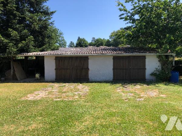 Une maison en pierres, jardin autour avec un abri de jardin et deux garages non attenants.