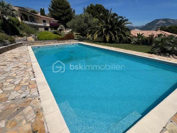Découvrez cette propriété d’exception où élégance, volumes et douceur de vivre se rencontrent dans un cadre privilégié.

Édifiée sur un magnifique terrain de 3 939 m², cette villa de prestige développe près de 240 m² habitables, répartis entre une villa principale de plain-pied de 160 m² et une dépendance indépendante de 80 m². Un lieu pensé pour ceux qui recherchent espace, confort et sérénité, avec une vue dégagée remarquable sur les montagnes, la ville et la mer.

Dès l’entrée, la lumière s’invite naturellement grâce aux larges baies vitrées qui habillent le spacieux séjour et prolongent les espaces vers une terrasse généreuse et un jardin soigneusement aménagé. Son exposition Sud-Est sublime chaque instant de la journée.

Le salon s’ouvre harmonieusement sur une cuisine moderne, entièrement équipée et ouverte sur l’espace de vie.

L’espace nuit propose trois belles chambres, dont une superbe suite parentale avec dressing et salle de bain privative, complétées par une salle d’eau, deux WC, une buanderie ainsi qu’un bureau donnant accès au garage.

Au niveau inférieur, une dépendance indépendante de 80 m² offre de nombreuses possibilités : recevoir famille et amis, activité professionnelle ou investissement locatif. Elle se compose d’un vaste séjour avec cheminée et cuisine américaine, d’une suite parentale avec salle d’eau et rangements, ainsi que d’un accès à une cave et un espace extérieur de stockage.

Les extérieurs ont été pensés comme une véritable invitation à la détente : une grande piscine 12 x 6, un élégant pool house avec cuisine d’été, douche, WC et local technique, plusieurs espaces de repos, un terrain de pétanque et de vastes espaces verts.

Deux garages ainsi que de nombreux stationnements complètent ce bien rare.

Prestations supplémentaires : classement énergétique A, panneaux solaires, arrosage automatique, goutte-à-goutte, fosse septique, cuve à gaz, eau du Canal de Provence.

Un lieu où les réveils commencent avec une vue inspirante et où les journées semblent toujours avoir un parfum de vacances.

Un véritable havre de paix à découvrir sans tarder.