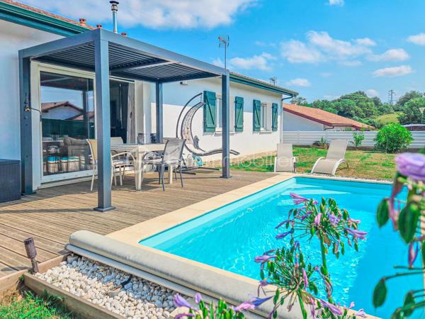 Maison contemporaine de plain-pied avec piscine – 4 chambres – Proche Bayonne

  Un véritable coup de cœur à découvrir sans tarder !

Dans un environnement calme et résidentiel, découvrez cette jolie maison contemporaine de 2017, 
entièrement de plain-pied, implantée sur une parcelle clôturée de 413 m².

Idéalement située, vous serez à seulement  5 minutes du centre commercial Ametzondo et 10 minutes de Bayonne.

    - VISITE VIRTUELLE SUR DEMANDE - GRATUITE

Dès l'entrée, vous serez séduits par une belle pièce de vie lumineuse de 43 m², chaleureuse et conviviale, 
agrémentée d'un poêle à granulés. 
Elle s'ouvre directement sur les extérieurs et la piscine.

La cuisine ouverte, aménagée et équipée, s'intègre parfaitement à cet espace de vie pensé pour profiter pleinement 
des moments en famille ou entre amis.

Un espace nuit confortable :

La maison propose 4 chambres, dont une belle **suite parentale** avec :

* dressing,
* salle d'eau avec douche à l'italienne,
* WC.

Un cellier avec accès au garage, une seconde salle d'eau et un WC indépendant viennent compléter l'espace intérieur.

Un extérieur pensé pour profiter pleinement des beaux jours.

Vous apprécierez particulièrement son jardin clos et facile à vivre, ainsi que ses deux terrasses exposées Sud-Ouest.

L'une bénéficie d'une pergola, l'autre d'un store, permettant de profiter des extérieurs à différents moments de la journée.

Et pour les journées ensoleillées : place à la détente avec une piscine chauffée et équipée d'une filtration au sel ! 

Un garage de 15 m² complète l'ensemble.

Les prestations : 

* Maison récente de 2017
* Plain-pied
* 4 chambres
* Piscine chauffée avec filtration au sel
* Poêle à granulés + chauffage électrique
* Eau chaude par ballon thermodynamique
* Huisseries PVC double vitrage
* Volets roulants électriques et bois
* VMC
* Moustiquaires
* Fibre
* Tout-à-l'égout
* Garage de 15 m²

  Les + qui font la différence :

Plain-pied • Maison récente • Excellent diagnostic performance énergétique classé en A et A • 4 chambres • Piscine • Jardin clos
• Terrasses • Calme • Proximité Bayonne

Une maison fonctionnelle, lumineuse et parfaitement adaptée à une vie de famille, où tout est réuni pour profiter 
d'un cadre de vie agréable à proximité immédiate de Bayonne.

Une maison coup de cœur qui ne devrait pas rester longtemps sur le marché… Alors, ne tardez pas !

 Je suis à votre écoute 7 jours sur 7 et m'adapte à votre planning pour organiser votre visite.