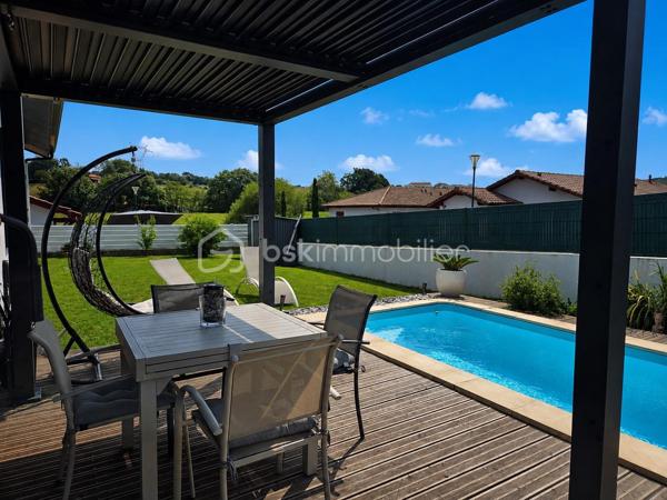 Maison contemporaine de plain-pied avec piscine – 4 chambres – Proche Bayonne

  Un véritable coup de cœur à découvrir sans tarder !

Dans un environnement calme et résidentiel, découvrez cette jolie maison contemporaine de 2017, 
entièrement de plain-pied, implantée sur une parcelle clôturée de 413 m².

Idéalement située, vous serez à seulement  5 minutes du centre commercial Ametzondo et 10 minutes de Bayonne.

    - VISITE VIRTUELLE SUR DEMANDE - GRATUITE

Dès l'entrée, vous serez séduits par une belle pièce de vie lumineuse de 43 m², chaleureuse et conviviale, 
agrémentée d'un poêle à granulés. 
Elle s'ouvre directement sur les extérieurs et la piscine.

La cuisine ouverte, aménagée et équipée, s'intègre parfaitement à cet espace de vie pensé pour profiter pleinement 
des moments en famille ou entre amis.

Un espace nuit confortable :

La maison propose 4 chambres, dont une belle **suite parentale** avec :

* dressing,
* salle d'eau avec douche à l'italienne,
* WC.

Un cellier avec accès au garage, une seconde salle d'eau et un WC indépendant viennent compléter l'espace intérieur.

Un extérieur pensé pour profiter pleinement des beaux jours.

Vous apprécierez particulièrement son jardin clos et facile à vivre, ainsi que ses deux terrasses exposées Sud-Ouest.

L'une bénéficie d'une pergola, l'autre d'un store, permettant de profiter des extérieurs à différents moments de la journée.

Et pour les journées ensoleillées : place à la détente avec une piscine chauffée et équipée d'une filtration au sel ! 

Un garage de 15 m² complète l'ensemble.

Les prestations : 

* Maison récente de 2017
* Plain-pied
* 4 chambres
* Piscine chauffée avec filtration au sel
* Poêle à granulés + chauffage électrique
* Eau chaude par ballon thermodynamique
* Huisseries PVC double vitrage
* Volets roulants électriques et bois
* VMC
* Moustiquaires
* Fibre
* Tout-à-l'égout
* Garage de 15 m²

  Les + qui font la différence :

Plain-pied • Maison récente • Excellent diagnostic performance énergétique classé en A et A • 4 chambres • Piscine • Jardin clos
• Terrasses • Calme • Proximité Bayonne

Une maison fonctionnelle, lumineuse et parfaitement adaptée à une vie de famille, où tout est réuni pour profiter 
d'un cadre de vie agréable à proximité immédiate de Bayonne.

Une maison coup de cœur qui ne devrait pas rester longtemps sur le marché… Alors, ne tardez pas !

 Je suis à votre écoute 7 jours sur 7 et m'adapte à votre planning pour organiser votre visite.