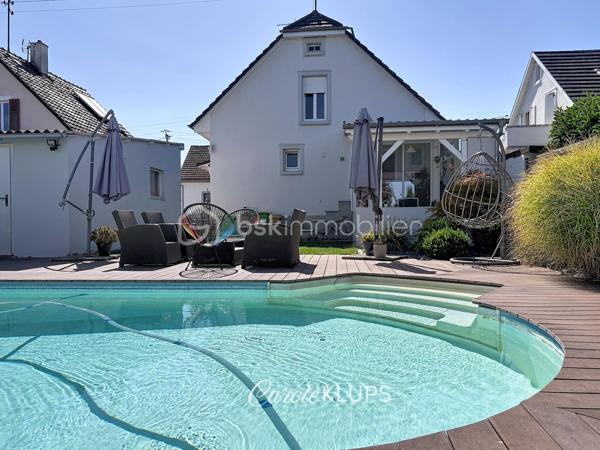 Maison familiale avec véranda, terrasse couverte, jardin et piscine à Village-Neuf

Ici, la surface habitable ne raconte pas tout. 112 m² habitables auxquels s’ajoutent une véranda d’environ 10 m², une terrasse couverte tournée vers le jardin, un sous-sol et un double garage. 

Le charme d’une maison des années 30 dans laquelle on peut se créer une véritable vie dedans-dehors, à deux pas de la frontière bâloise. Et pour les frontaliers, Bâle est accessible à vélo via la piste cyclable longeant le canal de Huningue.

Depuis la rue, on ne soupçonne pas le cadre de vie que cette maison réserve à l’arrière.

Résolument tournée vers l’extérieur, elle s’ouvre sur un jardin intimiste où chaque espace trouve naturellement sa place. Une belle terrasse couverte pour les repas entre amis ou en famille. À moins que vous ne préfériez vous installer au bord de la piscine chauffée … Autour, l’espace paysager invite au repos et à la convivialité.

Une sensation de vacances chez soi, avec un autre avantage appréciable : un jardin aux dimensions raisonnables, pensé pour en profiter sans devenir esclave de son entretien. Un puits présent sur la propriété permet par ailleurs d’assurer l’arrosage du jardin.

À l’intérieur aussi, chaque espace a sa fonction et la circulation est fluide.

Au rez-de-chaussée, le séjour de 32,6 m² invite à se prélasser près du poêle à bois. La cuisine équipée de 12 m² offre un espace confortable pour cuisiner, tandis que la véranda d’environ 10 m² devient naturellement une pièce supplémentaire pour partager les repas, avec le jardin en toile de fond.

Le + de ce rez-de-chaussée ? Une salle d’eau avec WC.

En montant à l’étage, même le palier a été optimisé avec un petit espace buanderie astucieusement dissimulé.

Puis vient l’une des belles surprises de la maison : une vaste mezzanine de plus de 23 m².

Aujourd’hui ouverte, elle sera votre terrain de jeu. Espace télétravail, bibliothèque, salle de jeux pour les enfants, salon télé… à chacun d’imaginer sa façon de l’habiter. Elle pourra également être cloisonnée pour créer une troisième chambre, qui viendra alors compléter les deux chambres existantes de 12,6 et 11,2 m².

La salle de bains de 7,6 m², avec baignoire, double vasque et WC, est quant à elle dimensionnée pour ces matins en famille où l’on apprécie de ne pas se marcher dessus.

Et ce n’est pas tout.

Au sous-sol, on retrouve une partie chaufferie, un atelier ainsi qu’un espace déjà aménagé en salle de sport, à conserver tel quel ou à réinventer selon vos besoins.

À l’extérieur, le double garage, la piscine chauffée et son local technique indépendant complètent les prestations de la maison.

Le tout prend place sur une parcelle de 480 m².

Enfin, sa situation en zone frontalière, avec des accès faciles vers la Suisse comme vers l’Allemagne, est particulièrement adaptée à la vie quotidienne des actifs du secteur.

Une maison avec jardin et piscine, une vraie vie dedans-dehors et Bâle à portée de vélo : profiter pleinement de chez soi sans renoncer à la proximité de la frontière.