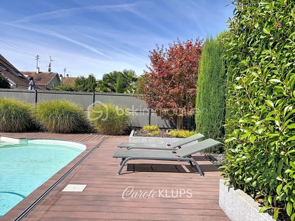 Maison familiale avec véranda, terrasse couverte, jardin et piscine à Village-Neuf

Ici, la surface habitable ne raconte pas tout. 112 m² habitables auxquels s’ajoutent une véranda d’environ 10 m², une terrasse couverte tournée vers le jardin, un sous-sol et un double garage. 

Le charme d’une maison des années 30 dans laquelle on peut se créer une véritable vie dedans-dehors, à deux pas de la frontière bâloise. Et pour les frontaliers, Bâle est accessible à vélo via la piste cyclable longeant le canal de Huningue.

Depuis la rue, on ne soupçonne pas le cadre de vie que cette maison réserve à l’arrière.

Résolument tournée vers l’extérieur, elle s’ouvre sur un jardin intimiste où chaque espace trouve naturellement sa place. Une belle terrasse couverte pour les repas entre amis ou en famille. À moins que vous ne préfériez vous installer au bord de la piscine chauffée … Autour, l’espace paysager invite au repos et à la convivialité.

Une sensation de vacances chez soi, avec un autre avantage appréciable : un jardin aux dimensions raisonnables, pensé pour en profiter sans devenir esclave de son entretien. Un puits présent sur la propriété permet par ailleurs d’assurer l’arrosage du jardin.

À l’intérieur aussi, chaque espace a sa fonction et la circulation est fluide.

Au rez-de-chaussée, le séjour de 32,6 m² invite à se prélasser près du poêle à bois. La cuisine équipée de 12 m² offre un espace confortable pour cuisiner, tandis que la véranda d’environ 10 m² devient naturellement une pièce supplémentaire pour partager les repas, avec le jardin en toile de fond.

Le + de ce rez-de-chaussée ? Une salle d’eau avec WC.

En montant à l’étage, même le palier a été optimisé avec un petit espace buanderie astucieusement dissimulé.

Puis vient l’une des belles surprises de la maison : une vaste mezzanine de plus de 23 m².

Aujourd’hui ouverte, elle sera votre terrain de jeu. Espace télétravail, bibliothèque, salle de jeux pour les enfants, salon télé… à chacun d’imaginer sa façon de l’habiter. Elle pourra également être cloisonnée pour créer une troisième chambre, qui viendra alors compléter les deux chambres existantes de 12,6 et 11,2 m².

La salle de bains de 7,6 m², avec baignoire, double vasque et WC, est quant à elle dimensionnée pour ces matins en famille où l’on apprécie de ne pas se marcher dessus.

Et ce n’est pas tout.

Au sous-sol, on retrouve une partie chaufferie, un atelier ainsi qu’un espace déjà aménagé en salle de sport, à conserver tel quel ou à réinventer selon vos besoins.

À l’extérieur, le double garage, la piscine chauffée et son local technique indépendant complètent les prestations de la maison.

Le tout prend place sur une parcelle de 480 m².

Enfin, sa situation en zone frontalière, avec des accès faciles vers la Suisse comme vers l’Allemagne, est particulièrement adaptée à la vie quotidienne des actifs du secteur.

Une maison avec jardin et piscine, une vraie vie dedans-dehors et Bâle à portée de vélo : profiter pleinement de chez soi sans renoncer à la proximité de la frontière.
