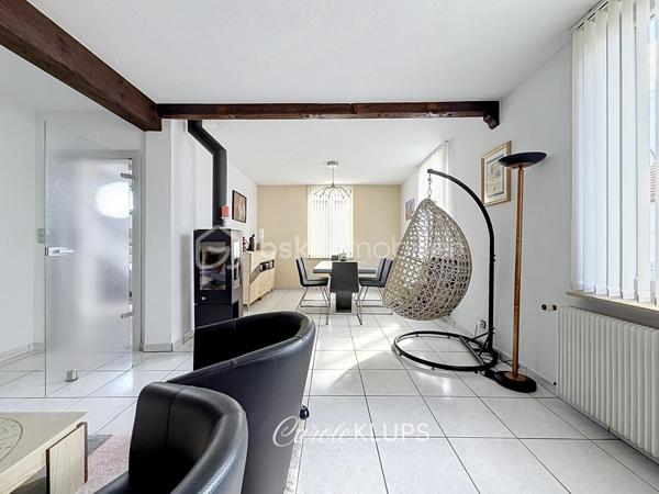 Maison familiale avec véranda, terrasse couverte, jardin et piscine à Village-Neuf

Ici, la surface habitable ne raconte pas tout. 112 m² habitables auxquels s’ajoutent une véranda d’environ 10 m², une terrasse couverte tournée vers le jardin, un sous-sol et un double garage. 

Le charme d’une maison des années 30 dans laquelle on peut se créer une véritable vie dedans-dehors, à deux pas de la frontière bâloise. Et pour les frontaliers, Bâle est accessible à vélo via la piste cyclable longeant le canal de Huningue.

Depuis la rue, on ne soupçonne pas le cadre de vie que cette maison réserve à l’arrière.

Résolument tournée vers l’extérieur, elle s’ouvre sur un jardin intimiste où chaque espace trouve naturellement sa place. Une belle terrasse couverte pour les repas entre amis ou en famille. À moins que vous ne préfériez vous installer au bord de la piscine chauffée … Autour, l’espace paysager invite au repos et à la convivialité.

Une sensation de vacances chez soi, avec un autre avantage appréciable : un jardin aux dimensions raisonnables, pensé pour en profiter sans devenir esclave de son entretien. Un puits présent sur la propriété permet par ailleurs d’assurer l’arrosage du jardin.

À l’intérieur aussi, chaque espace a sa fonction et la circulation est fluide.

Au rez-de-chaussée, le séjour de 32,6 m² invite à se prélasser près du poêle à bois. La cuisine équipée de 12 m² offre un espace confortable pour cuisiner, tandis que la véranda d’environ 10 m² devient naturellement une pièce supplémentaire pour partager les repas, avec le jardin en toile de fond.

Le + de ce rez-de-chaussée ? Une salle d’eau avec WC.

En montant à l’étage, même le palier a été optimisé avec un petit espace buanderie astucieusement dissimulé.

Puis vient l’une des belles surprises de la maison : une vaste mezzanine de plus de 23 m².

Aujourd’hui ouverte, elle sera votre terrain de jeu. Espace télétravail, bibliothèque, salle de jeux pour les enfants, salon télé… à chacun d’imaginer sa façon de l’habiter. Elle pourra également être cloisonnée pour créer une troisième chambre, qui viendra alors compléter les deux chambres existantes de 12,6 et 11,2 m².

La salle de bains de 7,6 m², avec baignoire, double vasque et WC, est quant à elle dimensionnée pour ces matins en famille où l’on apprécie de ne pas se marcher dessus.

Et ce n’est pas tout.

Au sous-sol, on retrouve une partie chaufferie, un atelier ainsi qu’un espace déjà aménagé en salle de sport, à conserver tel quel ou à réinventer selon vos besoins.

À l’extérieur, le double garage, la piscine chauffée et son local technique indépendant complètent les prestations de la maison.

Le tout prend place sur une parcelle de 480 m².

Enfin, sa situation en zone frontalière, avec des accès faciles vers la Suisse comme vers l’Allemagne, est particulièrement adaptée à la vie quotidienne des actifs du secteur.

Une maison avec jardin et piscine, une vraie vie dedans-dehors et Bâle à portée de vélo : profiter pleinement de chez soi sans renoncer à la proximité de la frontière.