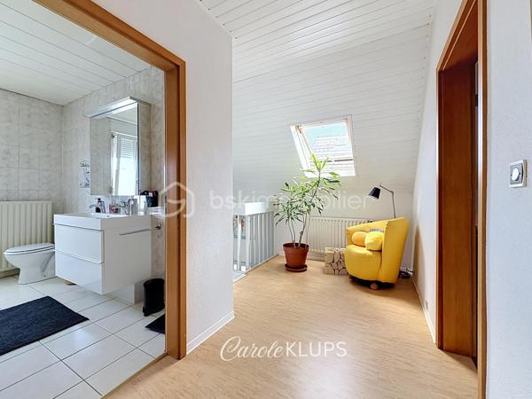 Maison familiale avec véranda, terrasse couverte, jardin et piscine à Village-Neuf

Ici, la surface habitable ne raconte pas tout. 112 m² habitables auxquels s’ajoutent une véranda d’environ 10 m², une terrasse couverte tournée vers le jardin, un sous-sol et un double garage. 

Le charme d’une maison des années 30 dans laquelle on peut se créer une véritable vie dedans-dehors, à deux pas de la frontière bâloise. Et pour les frontaliers, Bâle est accessible à vélo via la piste cyclable longeant le canal de Huningue.

Depuis la rue, on ne soupçonne pas le cadre de vie que cette maison réserve à l’arrière.

Résolument tournée vers l’extérieur, elle s’ouvre sur un jardin intimiste où chaque espace trouve naturellement sa place. Une belle terrasse couverte pour les repas entre amis ou en famille. À moins que vous ne préfériez vous installer au bord de la piscine chauffée … Autour, l’espace paysager invite au repos et à la convivialité.

Une sensation de vacances chez soi, avec un autre avantage appréciable : un jardin aux dimensions raisonnables, pensé pour en profiter sans devenir esclave de son entretien. Un puits présent sur la propriété permet par ailleurs d’assurer l’arrosage du jardin.

À l’intérieur aussi, chaque espace a sa fonction et la circulation est fluide.

Au rez-de-chaussée, le séjour de 32,6 m² invite à se prélasser près du poêle à bois. La cuisine équipée de 12 m² offre un espace confortable pour cuisiner, tandis que la véranda d’environ 10 m² devient naturellement une pièce supplémentaire pour partager les repas, avec le jardin en toile de fond.

Le + de ce rez-de-chaussée ? Une salle d’eau avec WC.

En montant à l’étage, même le palier a été optimisé avec un petit espace buanderie astucieusement dissimulé.

Puis vient l’une des belles surprises de la maison : une vaste mezzanine de plus de 23 m².

Aujourd’hui ouverte, elle sera votre terrain de jeu. Espace télétravail, bibliothèque, salle de jeux pour les enfants, salon télé… à chacun d’imaginer sa façon de l’habiter. Elle pourra également être cloisonnée pour créer une troisième chambre, qui viendra alors compléter les deux chambres existantes de 12,6 et 11,2 m².

La salle de bains de 7,6 m², avec baignoire, double vasque et WC, est quant à elle dimensionnée pour ces matins en famille où l’on apprécie de ne pas se marcher dessus.

Et ce n’est pas tout.

Au sous-sol, on retrouve une partie chaufferie, un atelier ainsi qu’un espace déjà aménagé en salle de sport, à conserver tel quel ou à réinventer selon vos besoins.

À l’extérieur, le double garage, la piscine chauffée et son local technique indépendant complètent les prestations de la maison.

Le tout prend place sur une parcelle de 480 m².

Enfin, sa situation en zone frontalière, avec des accès faciles vers la Suisse comme vers l’Allemagne, est particulièrement adaptée à la vie quotidienne des actifs du secteur.

Une maison avec jardin et piscine, une vraie vie dedans-dehors et Bâle à portée de vélo : profiter pleinement de chez soi sans renoncer à la proximité de la frontière.