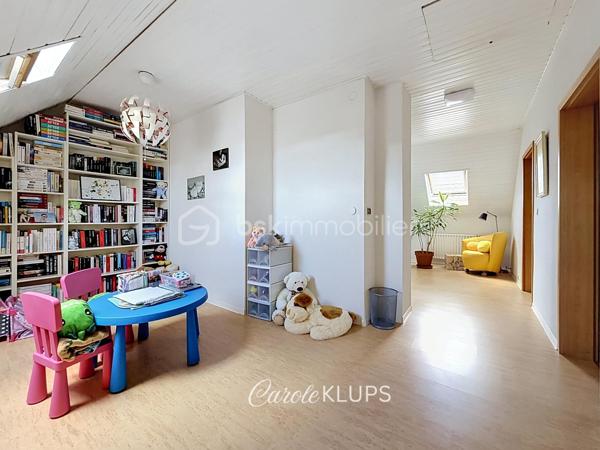 Maison familiale avec véranda, terrasse couverte, jardin et piscine à Village-Neuf

Ici, la surface habitable ne raconte pas tout. 112 m² habitables auxquels s’ajoutent une véranda d’environ 10 m², une terrasse couverte tournée vers le jardin, un sous-sol et un double garage. 

Le charme d’une maison des années 30 dans laquelle on peut se créer une véritable vie dedans-dehors, à deux pas de la frontière bâloise. Et pour les frontaliers, Bâle est accessible à vélo via la piste cyclable longeant le canal de Huningue.

Depuis la rue, on ne soupçonne pas le cadre de vie que cette maison réserve à l’arrière.

Résolument tournée vers l’extérieur, elle s’ouvre sur un jardin intimiste où chaque espace trouve naturellement sa place. Une belle terrasse couverte pour les repas entre amis ou en famille. À moins que vous ne préfériez vous installer au bord de la piscine chauffée … Autour, l’espace paysager invite au repos et à la convivialité.

Une sensation de vacances chez soi, avec un autre avantage appréciable : un jardin aux dimensions raisonnables, pensé pour en profiter sans devenir esclave de son entretien. Un puits présent sur la propriété permet par ailleurs d’assurer l’arrosage du jardin.

À l’intérieur aussi, chaque espace a sa fonction et la circulation est fluide.

Au rez-de-chaussée, le séjour de 32,6 m² invite à se prélasser près du poêle à bois. La cuisine équipée de 12 m² offre un espace confortable pour cuisiner, tandis que la véranda d’environ 10 m² devient naturellement une pièce supplémentaire pour partager les repas, avec le jardin en toile de fond.

Le + de ce rez-de-chaussée ? Une salle d’eau avec WC.

En montant à l’étage, même le palier a été optimisé avec un petit espace buanderie astucieusement dissimulé.

Puis vient l’une des belles surprises de la maison : une vaste mezzanine de plus de 23 m².

Aujourd’hui ouverte, elle sera votre terrain de jeu. Espace télétravail, bibliothèque, salle de jeux pour les enfants, salon télé… à chacun d’imaginer sa façon de l’habiter. Elle pourra également être cloisonnée pour créer une troisième chambre, qui viendra alors compléter les deux chambres existantes de 12,6 et 11,2 m².

La salle de bains de 7,6 m², avec baignoire, double vasque et WC, est quant à elle dimensionnée pour ces matins en famille où l’on apprécie de ne pas se marcher dessus.

Et ce n’est pas tout.

Au sous-sol, on retrouve une partie chaufferie, un atelier ainsi qu’un espace déjà aménagé en salle de sport, à conserver tel quel ou à réinventer selon vos besoins.

À l’extérieur, le double garage, la piscine chauffée et son local technique indépendant complètent les prestations de la maison.

Le tout prend place sur une parcelle de 480 m².

Enfin, sa situation en zone frontalière, avec des accès faciles vers la Suisse comme vers l’Allemagne, est particulièrement adaptée à la vie quotidienne des actifs du secteur.

Une maison avec jardin et piscine, une vraie vie dedans-dehors et Bâle à portée de vélo : profiter pleinement de chez soi sans renoncer à la proximité de la frontière.