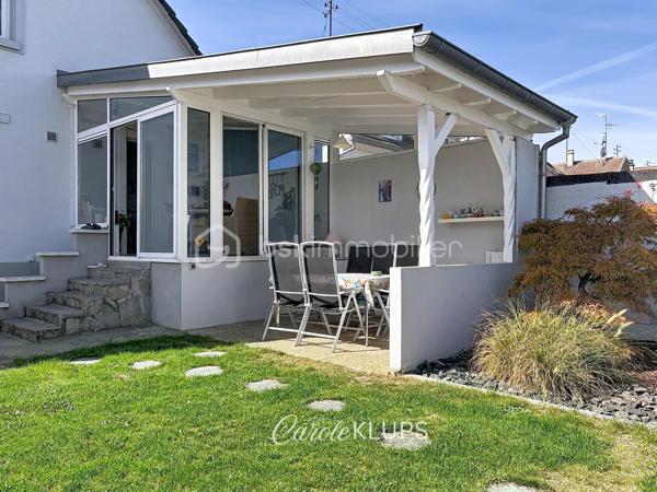 Maison familiale avec véranda, terrasse couverte, jardin et piscine à Village-Neuf

Ici, la surface habitable ne raconte pas tout. 112 m² habitables auxquels s’ajoutent une véranda d’environ 10 m², une terrasse couverte tournée vers le jardin, un sous-sol et un double garage. 

Le charme d’une maison des années 30 dans laquelle on peut se créer une véritable vie dedans-dehors, à deux pas de la frontière bâloise. Et pour les frontaliers, Bâle est accessible à vélo via la piste cyclable longeant le canal de Huningue.

Depuis la rue, on ne soupçonne pas le cadre de vie que cette maison réserve à l’arrière.

Résolument tournée vers l’extérieur, elle s’ouvre sur un jardin intimiste où chaque espace trouve naturellement sa place. Une belle terrasse couverte pour les repas entre amis ou en famille. À moins que vous ne préfériez vous installer au bord de la piscine chauffée … Autour, l’espace paysager invite au repos et à la convivialité.

Une sensation de vacances chez soi, avec un autre avantage appréciable : un jardin aux dimensions raisonnables, pensé pour en profiter sans devenir esclave de son entretien. Un puits présent sur la propriété permet par ailleurs d’assurer l’arrosage du jardin.

À l’intérieur aussi, chaque espace a sa fonction et la circulation est fluide.

Au rez-de-chaussée, le séjour de 32,6 m² invite à se prélasser près du poêle à bois. La cuisine équipée de 12 m² offre un espace confortable pour cuisiner, tandis que la véranda d’environ 10 m² devient naturellement une pièce supplémentaire pour partager les repas, avec le jardin en toile de fond.

Le + de ce rez-de-chaussée ? Une salle d’eau avec WC.

En montant à l’étage, même le palier a été optimisé avec un petit espace buanderie astucieusement dissimulé.

Puis vient l’une des belles surprises de la maison : une vaste mezzanine de plus de 23 m².

Aujourd’hui ouverte, elle sera votre terrain de jeu. Espace télétravail, bibliothèque, salle de jeux pour les enfants, salon télé… à chacun d’imaginer sa façon de l’habiter. Elle pourra également être cloisonnée pour créer une troisième chambre, qui viendra alors compléter les deux chambres existantes de 12,6 et 11,2 m².

La salle de bains de 7,6 m², avec baignoire, double vasque et WC, est quant à elle dimensionnée pour ces matins en famille où l’on apprécie de ne pas se marcher dessus.

Et ce n’est pas tout.

Au sous-sol, on retrouve une partie chaufferie, un atelier ainsi qu’un espace déjà aménagé en salle de sport, à conserver tel quel ou à réinventer selon vos besoins.

À l’extérieur, le double garage, la piscine chauffée et son local technique indépendant complètent les prestations de la maison.

Le tout prend place sur une parcelle de 480 m².

Enfin, sa situation en zone frontalière, avec des accès faciles vers la Suisse comme vers l’Allemagne, est particulièrement adaptée à la vie quotidienne des actifs du secteur.

Une maison avec jardin et piscine, une vraie vie dedans-dehors et Bâle à portée de vélo : profiter pleinement de chez soi sans renoncer à la proximité de la frontière.