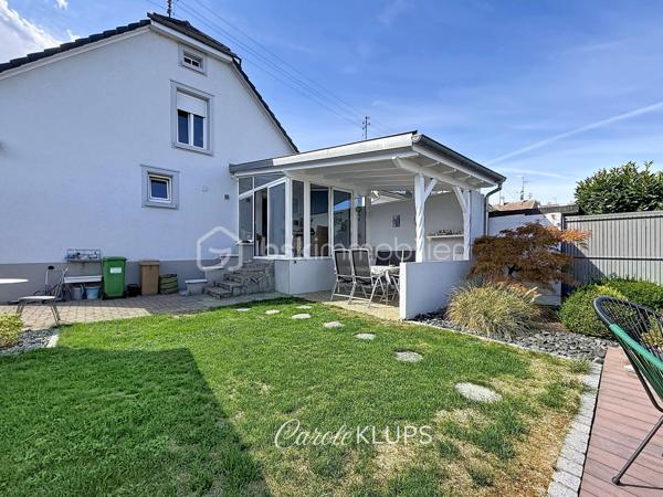 Maison familiale avec véranda, terrasse couverte, jardin et piscine à Village-Neuf

Ici, la surface habitable ne raconte pas tout. 112 m² habitables auxquels s’ajoutent une véranda d’environ 10 m², une terrasse couverte tournée vers le jardin, un sous-sol et un double garage. 

Le charme d’une maison des années 30 dans laquelle on peut se créer une véritable vie dedans-dehors, à deux pas de la frontière bâloise. Et pour les frontaliers, Bâle est accessible à vélo via la piste cyclable longeant le canal de Huningue.

Depuis la rue, on ne soupçonne pas le cadre de vie que cette maison réserve à l’arrière.

Résolument tournée vers l’extérieur, elle s’ouvre sur un jardin intimiste où chaque espace trouve naturellement sa place. Une belle terrasse couverte pour les repas entre amis ou en famille. À moins que vous ne préfériez vous installer au bord de la piscine chauffée … Autour, l’espace paysager invite au repos et à la convivialité.

Une sensation de vacances chez soi, avec un autre avantage appréciable : un jardin aux dimensions raisonnables, pensé pour en profiter sans devenir esclave de son entretien. Un puits présent sur la propriété permet par ailleurs d’assurer l’arrosage du jardin.

À l’intérieur aussi, chaque espace a sa fonction et la circulation est fluide.

Au rez-de-chaussée, le séjour de 32,6 m² invite à se prélasser près du poêle à bois. La cuisine équipée de 12 m² offre un espace confortable pour cuisiner, tandis que la véranda d’environ 10 m² devient naturellement une pièce supplémentaire pour partager les repas, avec le jardin en toile de fond.

Le + de ce rez-de-chaussée ? Une salle d’eau avec WC.

En montant à l’étage, même le palier a été optimisé avec un petit espace buanderie astucieusement dissimulé.

Puis vient l’une des belles surprises de la maison : une vaste mezzanine de plus de 23 m².

Aujourd’hui ouverte, elle sera votre terrain de jeu. Espace télétravail, bibliothèque, salle de jeux pour les enfants, salon télé… à chacun d’imaginer sa façon de l’habiter. Elle pourra également être cloisonnée pour créer une troisième chambre, qui viendra alors compléter les deux chambres existantes de 12,6 et 11,2 m².

La salle de bains de 7,6 m², avec baignoire, double vasque et WC, est quant à elle dimensionnée pour ces matins en famille où l’on apprécie de ne pas se marcher dessus.

Et ce n’est pas tout.

Au sous-sol, on retrouve une partie chaufferie, un atelier ainsi qu’un espace déjà aménagé en salle de sport, à conserver tel quel ou à réinventer selon vos besoins.

À l’extérieur, le double garage, la piscine chauffée et son local technique indépendant complètent les prestations de la maison.

Le tout prend place sur une parcelle de 480 m².

Enfin, sa situation en zone frontalière, avec des accès faciles vers la Suisse comme vers l’Allemagne, est particulièrement adaptée à la vie quotidienne des actifs du secteur.

Une maison avec jardin et piscine, une vraie vie dedans-dehors et Bâle à portée de vélo : profiter pleinement de chez soi sans renoncer à la proximité de la frontière.