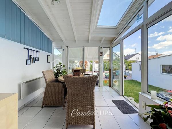 Maison familiale avec véranda, terrasse couverte, jardin et piscine à Village-Neuf

Ici, la surface habitable ne raconte pas tout. 112 m² habitables auxquels s’ajoutent une véranda d’environ 10 m², une terrasse couverte tournée vers le jardin, un sous-sol et un double garage. 

Le charme d’une maison des années 30 dans laquelle on peut se créer une véritable vie dedans-dehors, à deux pas de la frontière bâloise. Et pour les frontaliers, Bâle est accessible à vélo via la piste cyclable longeant le canal de Huningue.

Depuis la rue, on ne soupçonne pas le cadre de vie que cette maison réserve à l’arrière.

Résolument tournée vers l’extérieur, elle s’ouvre sur un jardin intimiste où chaque espace trouve naturellement sa place. Une belle terrasse couverte pour les repas entre amis ou en famille. À moins que vous ne préfériez vous installer au bord de la piscine chauffée … Autour, l’espace paysager invite au repos et à la convivialité.

Une sensation de vacances chez soi, avec un autre avantage appréciable : un jardin aux dimensions raisonnables, pensé pour en profiter sans devenir esclave de son entretien. Un puits présent sur la propriété permet par ailleurs d’assurer l’arrosage du jardin.

À l’intérieur aussi, chaque espace a sa fonction et la circulation est fluide.

Au rez-de-chaussée, le séjour de 32,6 m² invite à se prélasser près du poêle à bois. La cuisine équipée de 12 m² offre un espace confortable pour cuisiner, tandis que la véranda d’environ 10 m² devient naturellement une pièce supplémentaire pour partager les repas, avec le jardin en toile de fond.

Le + de ce rez-de-chaussée ? Une salle d’eau avec WC.

En montant à l’étage, même le palier a été optimisé avec un petit espace buanderie astucieusement dissimulé.

Puis vient l’une des belles surprises de la maison : une vaste mezzanine de plus de 23 m².

Aujourd’hui ouverte, elle sera votre terrain de jeu. Espace télétravail, bibliothèque, salle de jeux pour les enfants, salon télé… à chacun d’imaginer sa façon de l’habiter. Elle pourra également être cloisonnée pour créer une troisième chambre, qui viendra alors compléter les deux chambres existantes de 12,6 et 11,2 m².

La salle de bains de 7,6 m², avec baignoire, double vasque et WC, est quant à elle dimensionnée pour ces matins en famille où l’on apprécie de ne pas se marcher dessus.

Et ce n’est pas tout.

Au sous-sol, on retrouve une partie chaufferie, un atelier ainsi qu’un espace déjà aménagé en salle de sport, à conserver tel quel ou à réinventer selon vos besoins.

À l’extérieur, le double garage, la piscine chauffée et son local technique indépendant complètent les prestations de la maison.

Le tout prend place sur une parcelle de 480 m².

Enfin, sa situation en zone frontalière, avec des accès faciles vers la Suisse comme vers l’Allemagne, est particulièrement adaptée à la vie quotidienne des actifs du secteur.

Une maison avec jardin et piscine, une vraie vie dedans-dehors et Bâle à portée de vélo : profiter pleinement de chez soi sans renoncer à la proximité de la frontière.