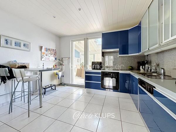 Maison familiale avec véranda, terrasse couverte, jardin et piscine à Village-Neuf

Ici, la surface habitable ne raconte pas tout. 112 m² habitables auxquels s’ajoutent une véranda d’environ 10 m², une terrasse couverte tournée vers le jardin, un sous-sol et un double garage. 

Le charme d’une maison des années 30 dans laquelle on peut se créer une véritable vie dedans-dehors, à deux pas de la frontière bâloise. Et pour les frontaliers, Bâle est accessible à vélo via la piste cyclable longeant le canal de Huningue.

Depuis la rue, on ne soupçonne pas le cadre de vie que cette maison réserve à l’arrière.

Résolument tournée vers l’extérieur, elle s’ouvre sur un jardin intimiste où chaque espace trouve naturellement sa place. Une belle terrasse couverte pour les repas entre amis ou en famille. À moins que vous ne préfériez vous installer au bord de la piscine chauffée … Autour, l’espace paysager invite au repos et à la convivialité.

Une sensation de vacances chez soi, avec un autre avantage appréciable : un jardin aux dimensions raisonnables, pensé pour en profiter sans devenir esclave de son entretien. Un puits présent sur la propriété permet par ailleurs d’assurer l’arrosage du jardin.

À l’intérieur aussi, chaque espace a sa fonction et la circulation est fluide.

Au rez-de-chaussée, le séjour de 32,6 m² invite à se prélasser près du poêle à bois. La cuisine équipée de 12 m² offre un espace confortable pour cuisiner, tandis que la véranda d’environ 10 m² devient naturellement une pièce supplémentaire pour partager les repas, avec le jardin en toile de fond.

Le + de ce rez-de-chaussée ? Une salle d’eau avec WC.

En montant à l’étage, même le palier a été optimisé avec un petit espace buanderie astucieusement dissimulé.

Puis vient l’une des belles surprises de la maison : une vaste mezzanine de plus de 23 m².

Aujourd’hui ouverte, elle sera votre terrain de jeu. Espace télétravail, bibliothèque, salle de jeux pour les enfants, salon télé… à chacun d’imaginer sa façon de l’habiter. Elle pourra également être cloisonnée pour créer une troisième chambre, qui viendra alors compléter les deux chambres existantes de 12,6 et 11,2 m².

La salle de bains de 7,6 m², avec baignoire, double vasque et WC, est quant à elle dimensionnée pour ces matins en famille où l’on apprécie de ne pas se marcher dessus.

Et ce n’est pas tout.

Au sous-sol, on retrouve une partie chaufferie, un atelier ainsi qu’un espace déjà aménagé en salle de sport, à conserver tel quel ou à réinventer selon vos besoins.

À l’extérieur, le double garage, la piscine chauffée et son local technique indépendant complètent les prestations de la maison.

Le tout prend place sur une parcelle de 480 m².

Enfin, sa situation en zone frontalière, avec des accès faciles vers la Suisse comme vers l’Allemagne, est particulièrement adaptée à la vie quotidienne des actifs du secteur.

Une maison avec jardin et piscine, une vraie vie dedans-dehors et Bâle à portée de vélo : profiter pleinement de chez soi sans renoncer à la proximité de la frontière.