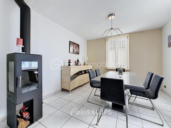 Maison familiale avec véranda, terrasse couverte, jardin et piscine à Village-Neuf

Ici, la surface habitable ne raconte pas tout. 112 m² habitables auxquels s’ajoutent une véranda d’environ 10 m², une terrasse couverte tournée vers le jardin, un sous-sol et un double garage. 

Le charme d’une maison des années 30 dans laquelle on peut se créer une véritable vie dedans-dehors, à deux pas de la frontière bâloise. Et pour les frontaliers, Bâle est accessible à vélo via la piste cyclable longeant le canal de Huningue.

Depuis la rue, on ne soupçonne pas le cadre de vie que cette maison réserve à l’arrière.

Résolument tournée vers l’extérieur, elle s’ouvre sur un jardin intimiste où chaque espace trouve naturellement sa place. Une belle terrasse couverte pour les repas entre amis ou en famille. À moins que vous ne préfériez vous installer au bord de la piscine chauffée … Autour, l’espace paysager invite au repos et à la convivialité.

Une sensation de vacances chez soi, avec un autre avantage appréciable : un jardin aux dimensions raisonnables, pensé pour en profiter sans devenir esclave de son entretien. Un puits présent sur la propriété permet par ailleurs d’assurer l’arrosage du jardin.

À l’intérieur aussi, chaque espace a sa fonction et la circulation est fluide.

Au rez-de-chaussée, le séjour de 32,6 m² invite à se prélasser près du poêle à bois. La cuisine équipée de 12 m² offre un espace confortable pour cuisiner, tandis que la véranda d’environ 10 m² devient naturellement une pièce supplémentaire pour partager les repas, avec le jardin en toile de fond.

Le + de ce rez-de-chaussée ? Une salle d’eau avec WC.

En montant à l’étage, même le palier a été optimisé avec un petit espace buanderie astucieusement dissimulé.

Puis vient l’une des belles surprises de la maison : une vaste mezzanine de plus de 23 m².

Aujourd’hui ouverte, elle sera votre terrain de jeu. Espace télétravail, bibliothèque, salle de jeux pour les enfants, salon télé… à chacun d’imaginer sa façon de l’habiter. Elle pourra également être cloisonnée pour créer une troisième chambre, qui viendra alors compléter les deux chambres existantes de 12,6 et 11,2 m².

La salle de bains de 7,6 m², avec baignoire, double vasque et WC, est quant à elle dimensionnée pour ces matins en famille où l’on apprécie de ne pas se marcher dessus.

Et ce n’est pas tout.

Au sous-sol, on retrouve une partie chaufferie, un atelier ainsi qu’un espace déjà aménagé en salle de sport, à conserver tel quel ou à réinventer selon vos besoins.

À l’extérieur, le double garage, la piscine chauffée et son local technique indépendant complètent les prestations de la maison.

Le tout prend place sur une parcelle de 480 m².

Enfin, sa situation en zone frontalière, avec des accès faciles vers la Suisse comme vers l’Allemagne, est particulièrement adaptée à la vie quotidienne des actifs du secteur.

Une maison avec jardin et piscine, une vraie vie dedans-dehors et Bâle à portée de vélo : profiter pleinement de chez soi sans renoncer à la proximité de la frontière.