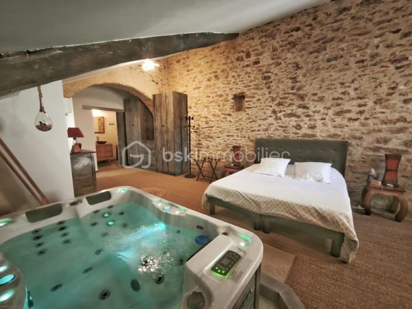 À l'entrée du village pittoresque de Faugères, au cœur d'un environnement réputé pour son vignoble AOP et sa qualité de vie, découvrez cette authentique maison en pierre de 179 m² habitables, organisée autour d'un agréable patio intérieur.
La propriété offre une configuration rare avec deux espaces de vie communicants : une habitation principale pleine de charme et une suite indépendante avec espace bien-être, idéale pour accueillir famille, amis, exercer une activité touristique ou créer un espace dédié au télétravail ou à une profession libérale.

L'habitation principale
L'entrée s'ouvre sur une spacieuse cuisine de 23 m², équipée d'une climatisation réversible et d'un poêle à granulés.
Elle mène à un superbe salon de 36 m², aménagé dans une ancienne écurie. Son plafond voûté, sa belle hauteur sous plafond et sa grande baie vitrée ouverte sur le patio lui confèrent un caractère unique.
Un WC indépendant complète le rez-de-chaussée, ainsi qu'un accès direct au garage de 35 m² équipé d'une porte motorisée.
À l'étage, une première chambre de 20,5 m² avec dressing (actuellement aménagée en bureau) précède une agréable suite parentale de 23,8 m² avec salle d'eau, double vasque, WC indépendant et climatisation.

La suite indépendante bien-être
Communicante avec la maison tout en bénéficiant d'un accès par le patio, cette seconde partie de la propriété comprend :
un salon / salle à manger de 33,65 m² avec climatisation et poêle à granulés ;
un WC indépendant ;
une vaste suite d'environ 40 m² avec salle d'eau ;
un jacuzzi privatif ;
un sauna dans une pièce attenante ;
une terrasse privée de 8 m².

Cet espace peut accueillir une activité de location saisonnière, recevoir famille et amis en toute autonomie ou encore être intégré à l'habitation principale.

Un extérieur intimiste
Véritable cœur de la maison, le patio de 31 m², à l'abri des regards, est accessible depuis les deux espaces de vie, le garage et la rue située à l'arrière de la propriété.
Il dispose d'une cuisine d'été de 5,6 m² ainsi que d'une buanderie de 5 m², parfaites pour profiter pleinement des beaux jours.

Les atouts
179 m² habitables
Deux espaces de vie communicants
Suite indépendante avec jacuzzi et sauna
Ancienne écurie rénovée avec salon voûté
Patio de 31 m²
Garage de 35 m²
Cuisine d'été
Climatisations réversibles
Deux poêles à granulés
Fibre optique
Faible taxe foncière 

Faugères offre un cadre de vie recherché entre vignobles et nature, avec école, commerces de proximité, restaurants et domaines viticoles. Béziers, Pézenas, les plages méditerranéennes et le Parc naturel régional du Haut-Languedoc sont rapidement accessibles.

Prix : 290 000 € HAI