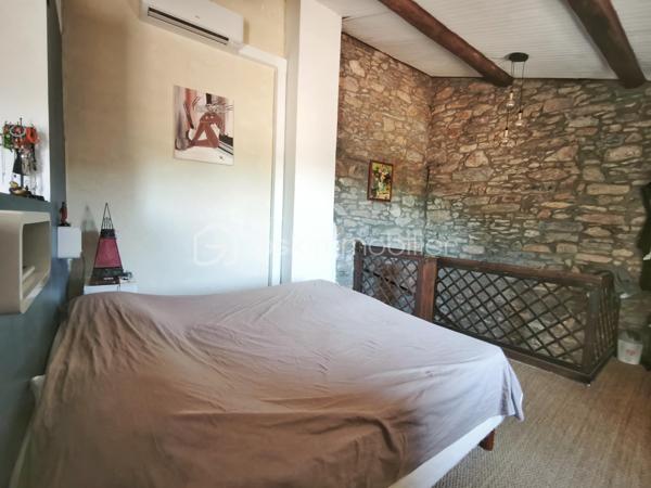 À l'entrée du village pittoresque de Faugères, au cœur d'un environnement réputé pour son vignoble AOP et sa qualité de vie, découvrez cette authentique maison en pierre de 179 m² habitables, organisée autour d'un agréable patio intérieur.
La propriété offre une configuration rare avec deux espaces de vie communicants : une habitation principale pleine de charme et une suite indépendante avec espace bien-être, idéale pour accueillir famille, amis, exercer une activité touristique ou créer un espace dédié au télétravail ou à une profession libérale.

L'habitation principale
L'entrée s'ouvre sur une spacieuse cuisine de 23 m², équipée d'une climatisation réversible et d'un poêle à granulés.
Elle mène à un superbe salon de 36 m², aménagé dans une ancienne écurie. Son plafond voûté, sa belle hauteur sous plafond et sa grande baie vitrée ouverte sur le patio lui confèrent un caractère unique.
Un WC indépendant complète le rez-de-chaussée, ainsi qu'un accès direct au garage de 35 m² équipé d'une porte motorisée.
À l'étage, une première chambre de 20,5 m² avec dressing (actuellement aménagée en bureau) précède une agréable suite parentale de 23,8 m² avec salle d'eau, double vasque, WC indépendant et climatisation.

La suite indépendante bien-être
Communicante avec la maison tout en bénéficiant d'un accès par le patio, cette seconde partie de la propriété comprend :
un salon / salle à manger de 33,65 m² avec climatisation et poêle à granulés ;
un WC indépendant ;
une vaste suite d'environ 40 m² avec salle d'eau ;
un jacuzzi privatif ;
un sauna dans une pièce attenante ;
une terrasse privée de 8 m².

Cet espace peut accueillir une activité de location saisonnière, recevoir famille et amis en toute autonomie ou encore être intégré à l'habitation principale.

Un extérieur intimiste
Véritable cœur de la maison, le patio de 31 m², à l'abri des regards, est accessible depuis les deux espaces de vie, le garage et la rue située à l'arrière de la propriété.
Il dispose d'une cuisine d'été de 5,6 m² ainsi que d'une buanderie de 5 m², parfaites pour profiter pleinement des beaux jours.

Les atouts
179 m² habitables
Deux espaces de vie communicants
Suite indépendante avec jacuzzi et sauna
Ancienne écurie rénovée avec salon voûté
Patio de 31 m²
Garage de 35 m²
Cuisine d'été
Climatisations réversibles
Deux poêles à granulés
Fibre optique
Faible taxe foncière 

Faugères offre un cadre de vie recherché entre vignobles et nature, avec école, commerces de proximité, restaurants et domaines viticoles. Béziers, Pézenas, les plages méditerranéennes et le Parc naturel régional du Haut-Languedoc sont rapidement accessibles.

Prix : 290 000 € HAI