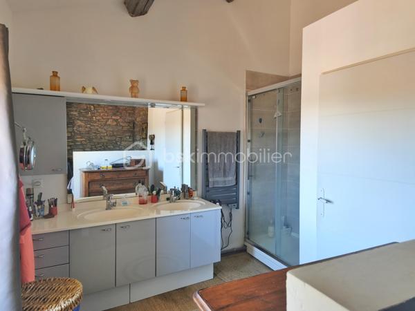 À l'entrée du village pittoresque de Faugères, au cœur d'un environnement réputé pour son vignoble AOP et sa qualité de vie, découvrez cette authentique maison en pierre de 179 m² habitables, organisée autour d'un agréable patio intérieur.
La propriété offre une configuration rare avec deux espaces de vie communicants : une habitation principale pleine de charme et une suite indépendante avec espace bien-être, idéale pour accueillir famille, amis, exercer une activité touristique ou créer un espace dédié au télétravail ou à une profession libérale.

L'habitation principale
L'entrée s'ouvre sur une spacieuse cuisine de 23 m², équipée d'une climatisation réversible et d'un poêle à granulés.
Elle mène à un superbe salon de 36 m², aménagé dans une ancienne écurie. Son plafond voûté, sa belle hauteur sous plafond et sa grande baie vitrée ouverte sur le patio lui confèrent un caractère unique.
Un WC indépendant complète le rez-de-chaussée, ainsi qu'un accès direct au garage de 35 m² équipé d'une porte motorisée.
À l'étage, une première chambre de 20,5 m² avec dressing (actuellement aménagée en bureau) précède une agréable suite parentale de 23,8 m² avec salle d'eau, double vasque, WC indépendant et climatisation.

La suite indépendante bien-être
Communicante avec la maison tout en bénéficiant d'un accès par le patio, cette seconde partie de la propriété comprend :
un salon / salle à manger de 33,65 m² avec climatisation et poêle à granulés ;
un WC indépendant ;
une vaste suite d'environ 40 m² avec salle d'eau ;
un jacuzzi privatif ;
un sauna dans une pièce attenante ;
une terrasse privée de 8 m².

Cet espace peut accueillir une activité de location saisonnière, recevoir famille et amis en toute autonomie ou encore être intégré à l'habitation principale.

Un extérieur intimiste
Véritable cœur de la maison, le patio de 31 m², à l'abri des regards, est accessible depuis les deux espaces de vie, le garage et la rue située à l'arrière de la propriété.
Il dispose d'une cuisine d'été de 5,6 m² ainsi que d'une buanderie de 5 m², parfaites pour profiter pleinement des beaux jours.

Les atouts
179 m² habitables
Deux espaces de vie communicants
Suite indépendante avec jacuzzi et sauna
Ancienne écurie rénovée avec salon voûté
Patio de 31 m²
Garage de 35 m²
Cuisine d'été
Climatisations réversibles
Deux poêles à granulés
Fibre optique
Faible taxe foncière 

Faugères offre un cadre de vie recherché entre vignobles et nature, avec école, commerces de proximité, restaurants et domaines viticoles. Béziers, Pézenas, les plages méditerranéennes et le Parc naturel régional du Haut-Languedoc sont rapidement accessibles.

Prix : 290 000 € HAI