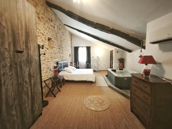 À l'entrée du village pittoresque de Faugères, au cœur d'un environnement réputé pour son vignoble AOP et sa qualité de vie, découvrez cette authentique maison en pierre de 179 m² habitables, organisée autour d'un agréable patio intérieur.
La propriété offre une configuration rare avec deux espaces de vie communicants : une habitation principale pleine de charme et une suite indépendante avec espace bien-être, idéale pour accueillir famille, amis, exercer une activité touristique ou créer un espace dédié au télétravail ou à une profession libérale.

L'habitation principale
L'entrée s'ouvre sur une spacieuse cuisine de 23 m², équipée d'une climatisation réversible et d'un poêle à granulés.
Elle mène à un superbe salon de 36 m², aménagé dans une ancienne écurie. Son plafond voûté, sa belle hauteur sous plafond et sa grande baie vitrée ouverte sur le patio lui confèrent un caractère unique.
Un WC indépendant complète le rez-de-chaussée, ainsi qu'un accès direct au garage de 35 m² équipé d'une porte motorisée.
À l'étage, une première chambre de 20,5 m² avec dressing (actuellement aménagée en bureau) précède une agréable suite parentale de 23,8 m² avec salle d'eau, double vasque, WC indépendant et climatisation.

La suite indépendante bien-être
Communicante avec la maison tout en bénéficiant d'un accès par le patio, cette seconde partie de la propriété comprend :
un salon / salle à manger de 33,65 m² avec climatisation et poêle à granulés ;
un WC indépendant ;
une vaste suite d'environ 40 m² avec salle d'eau ;
un jacuzzi privatif ;
un sauna dans une pièce attenante ;
une terrasse privée de 8 m².

Cet espace peut accueillir une activité de location saisonnière, recevoir famille et amis en toute autonomie ou encore être intégré à l'habitation principale.

Un extérieur intimiste
Véritable cœur de la maison, le patio de 31 m², à l'abri des regards, est accessible depuis les deux espaces de vie, le garage et la rue située à l'arrière de la propriété.
Il dispose d'une cuisine d'été de 5,6 m² ainsi que d'une buanderie de 5 m², parfaites pour profiter pleinement des beaux jours.

Les atouts
179 m² habitables
Deux espaces de vie communicants
Suite indépendante avec jacuzzi et sauna
Ancienne écurie rénovée avec salon voûté
Patio de 31 m²
Garage de 35 m²
Cuisine d'été
Climatisations réversibles
Deux poêles à granulés
Fibre optique
Faible taxe foncière 

Faugères offre un cadre de vie recherché entre vignobles et nature, avec école, commerces de proximité, restaurants et domaines viticoles. Béziers, Pézenas, les plages méditerranéennes et le Parc naturel régional du Haut-Languedoc sont rapidement accessibles.

Prix : 290 000 € HAI