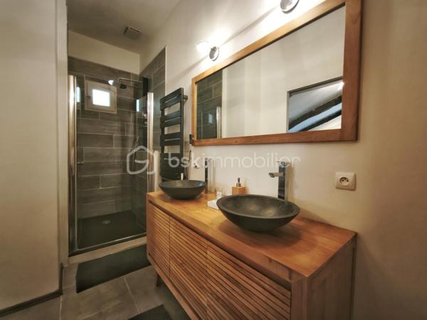À l'entrée du village pittoresque de Faugères, au cœur d'un environnement réputé pour son vignoble AOP et sa qualité de vie, découvrez cette authentique maison en pierre de 179 m² habitables, organisée autour d'un agréable patio intérieur.
La propriété offre une configuration rare avec deux espaces de vie communicants : une habitation principale pleine de charme et une suite indépendante avec espace bien-être, idéale pour accueillir famille, amis, exercer une activité touristique ou créer un espace dédié au télétravail ou à une profession libérale.

L'habitation principale
L'entrée s'ouvre sur une spacieuse cuisine de 23 m², équipée d'une climatisation réversible et d'un poêle à granulés.
Elle mène à un superbe salon de 36 m², aménagé dans une ancienne écurie. Son plafond voûté, sa belle hauteur sous plafond et sa grande baie vitrée ouverte sur le patio lui confèrent un caractère unique.
Un WC indépendant complète le rez-de-chaussée, ainsi qu'un accès direct au garage de 35 m² équipé d'une porte motorisée.
À l'étage, une première chambre de 20,5 m² avec dressing (actuellement aménagée en bureau) précède une agréable suite parentale de 23,8 m² avec salle d'eau, double vasque, WC indépendant et climatisation.

La suite indépendante bien-être
Communicante avec la maison tout en bénéficiant d'un accès par le patio, cette seconde partie de la propriété comprend :
un salon / salle à manger de 33,65 m² avec climatisation et poêle à granulés ;
un WC indépendant ;
une vaste suite d'environ 40 m² avec salle d'eau ;
un jacuzzi privatif ;
un sauna dans une pièce attenante ;
une terrasse privée de 8 m².

Cet espace peut accueillir une activité de location saisonnière, recevoir famille et amis en toute autonomie ou encore être intégré à l'habitation principale.

Un extérieur intimiste
Véritable cœur de la maison, le patio de 31 m², à l'abri des regards, est accessible depuis les deux espaces de vie, le garage et la rue située à l'arrière de la propriété.
Il dispose d'une cuisine d'été de 5,6 m² ainsi que d'une buanderie de 5 m², parfaites pour profiter pleinement des beaux jours.

Les atouts
179 m² habitables
Deux espaces de vie communicants
Suite indépendante avec jacuzzi et sauna
Ancienne écurie rénovée avec salon voûté
Patio de 31 m²
Garage de 35 m²
Cuisine d'été
Climatisations réversibles
Deux poêles à granulés
Fibre optique
Faible taxe foncière 

Faugères offre un cadre de vie recherché entre vignobles et nature, avec école, commerces de proximité, restaurants et domaines viticoles. Béziers, Pézenas, les plages méditerranéennes et le Parc naturel régional du Haut-Languedoc sont rapidement accessibles.

Prix : 290 000 € HAI