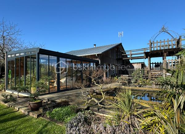 Rare à la vente, cet atelier d'artiste aménagé en maison d'habitation offre un beau potentiel à ses futurs propriétaires. 
Amoureux du bois et de la nature, ce "chalet" est fait pour vous ! Contrairement à ce que l'on pourrait penser, la structure de la maison n'est pas en bois mais en parpaing et a été enduite à la chaux. Ensuite un bardage bois a été posé. 
S'il reste aujourd'hui un atelier de peinture de 28m2 dans lequel vous pourriez aisément aussi y faire un bureau, une salle de sport, une salle de jeux ou un garage, 105m2 sont prêts à accueillir votre famille. 
Nous commencerons la visite par la pièce de vie de 45m2 qui comprend le salon-séjour et la cuisine. Une magnifique véranda chauffée "jardin d'hiver" complète cette maison, idéale pour y installer une grande table familiale ou encore un salon. 
Nous poursuivrons la visite du rez-de-chaussée avec une salle d'eau de 6m2, une chambre de 11m2. 
A l'étage, deux chambres de 12m2 au sol dont une donne accès à la "tour". 
Le mode de chauffage principal est un poêle à bois et radiateurs électriques dans la véranda et l'atelier. La maison consomme peu, le DPE est en C. 
Toutes les menuiseries sont en double vitrage. 
Coté rangement, belle surprise avec le sous-sol de 75m2, vous pourrez y stocker vélos, motos, outils et aisément un coin bricolage si vous le souhaitez. Pas de voiture possible. 
Une microstation a été installée. La toiture est en bac acier. 
Coté extérieur, vous pourrez profitez sans aucun vis à vis de la parcelle de 3300m2 partiellement close et joliment arborée et agrémentée tant par ses terrasses bois que par le bassin à poissons avec sa fontaine. 
Vous aimez le jardin, deux serres sont en place. 
La maison se situe aux portes de la Bretagne, à deux minutes de l'axe Laval-Rennes. 
Alors vous aussi vous aimez cette maison-atelier ? Appelez-moi pour plus de renseignements et peut-être fixer une visite !